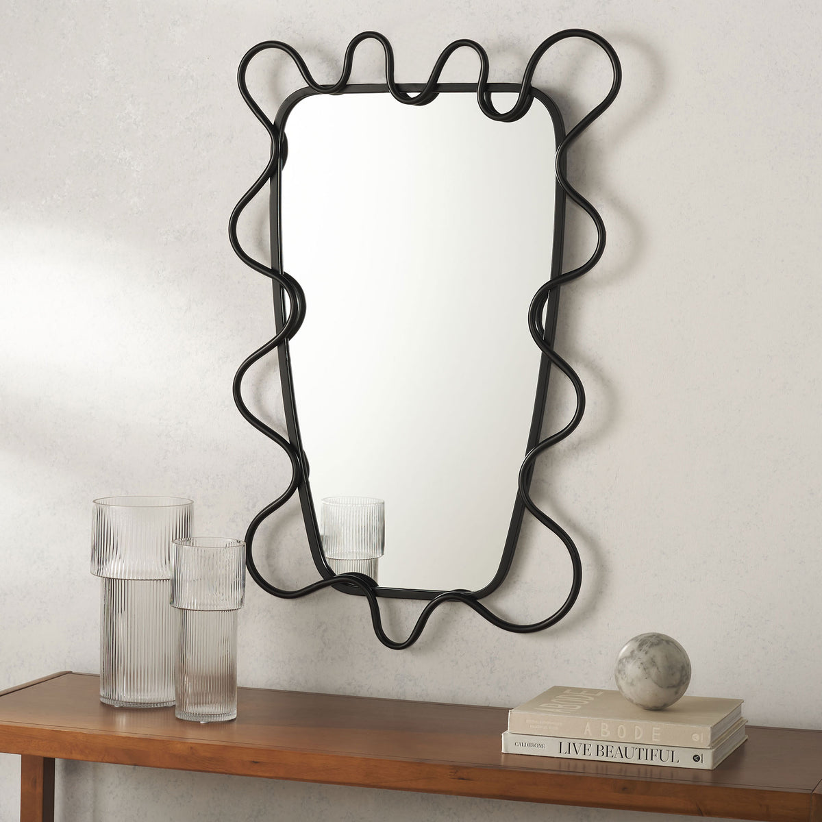 A tall mirror with flowing black metal trim brings sculptural style above a wood console || MRR2500A || front_room