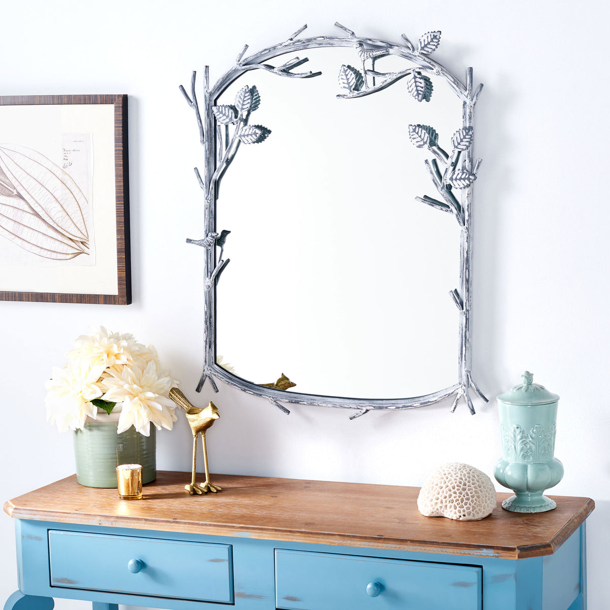 A silver mirror with sculpted branches brings a whimsical accent above a blue console. || MRR3042A || front_room