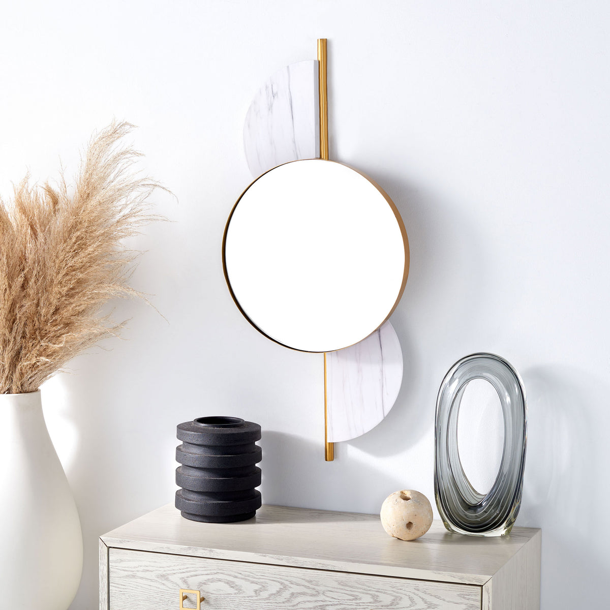A gold-framed round mirror with soft white veined accents brightens the wall above a pale console.