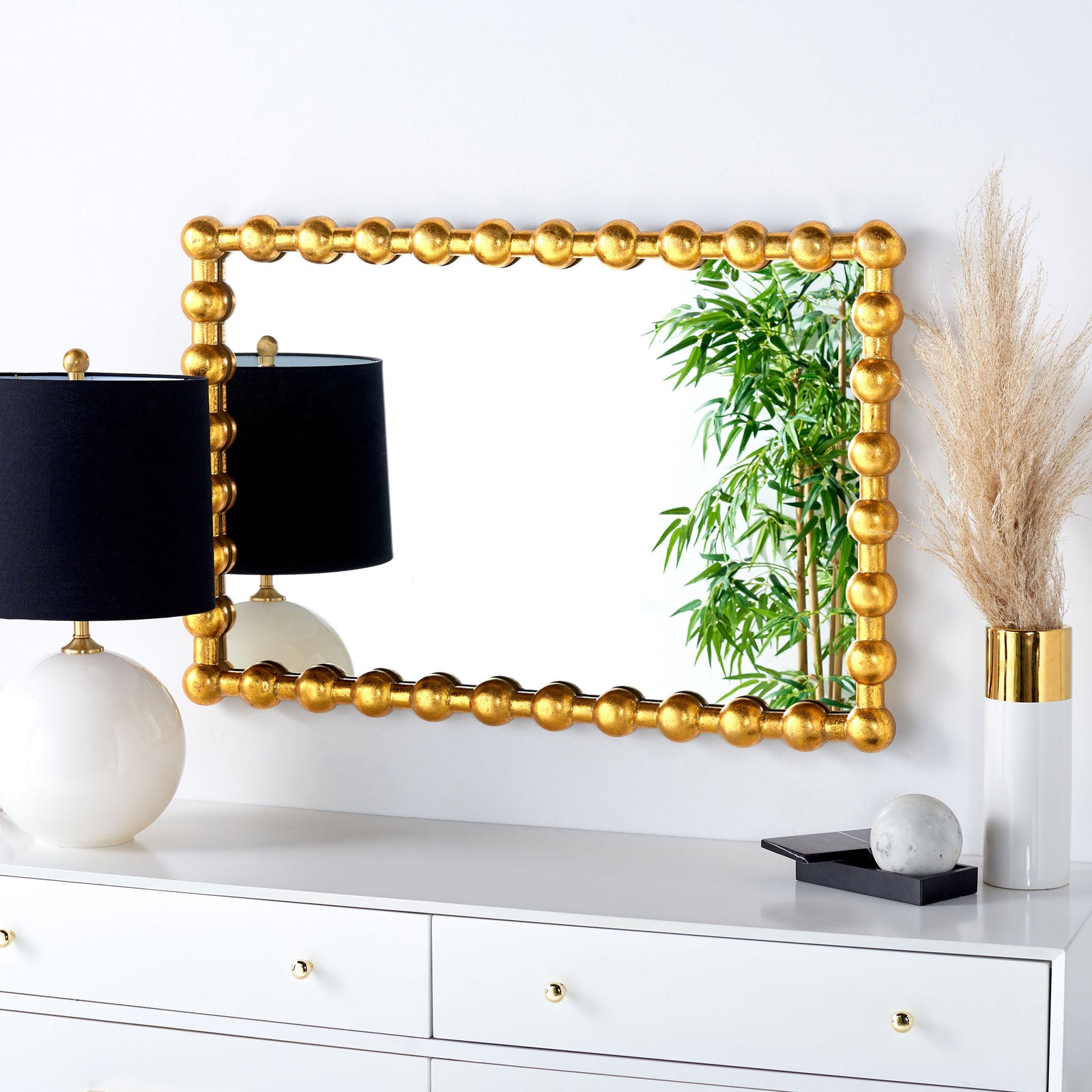 A gold beaded mirror adds warmth above a white dresser, reflecting leafy greenery. || MRR3055A || front_room