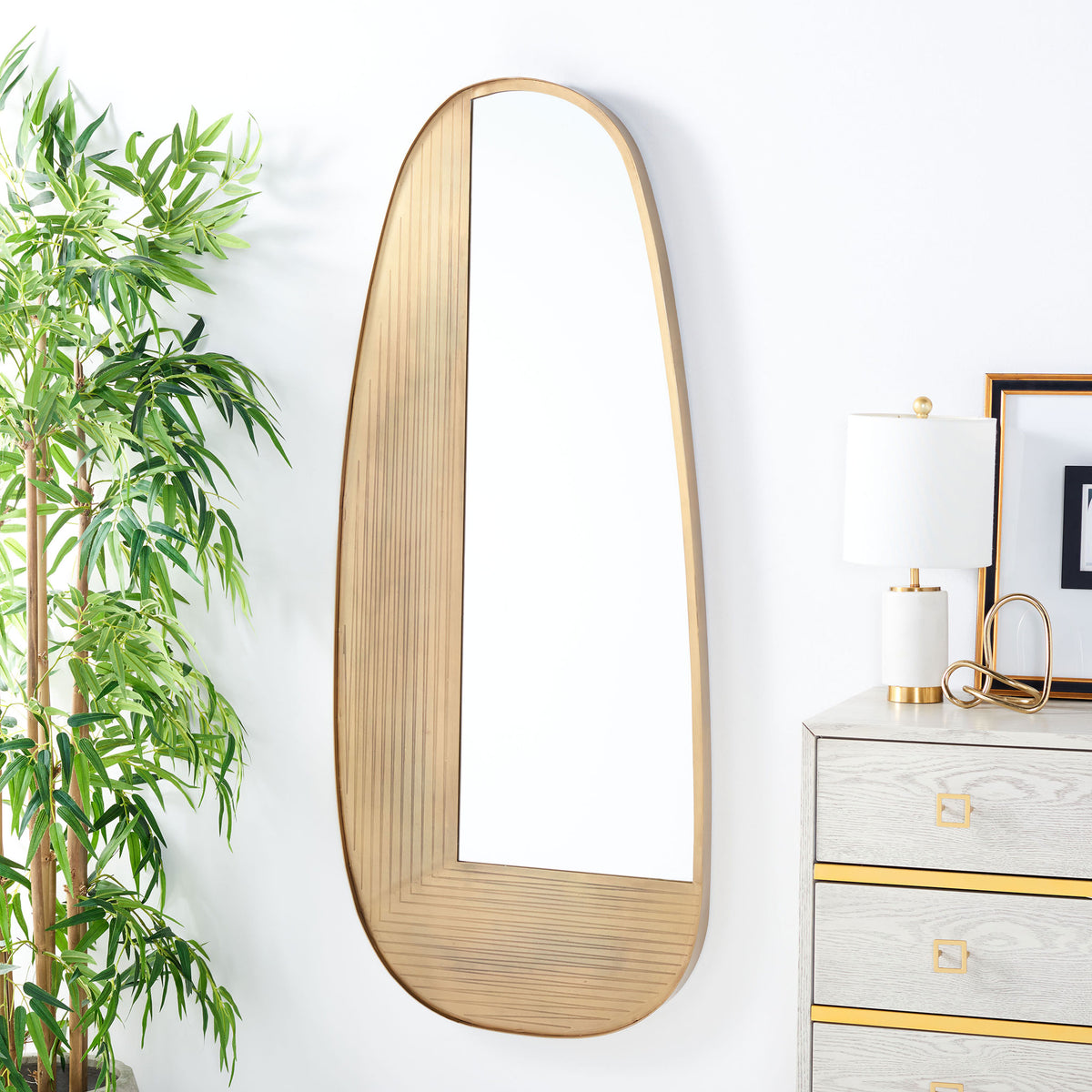 Curved brass-finish wall mirror adds sculptural warmth beside a light-toned dresser || MRR3067A || front_room