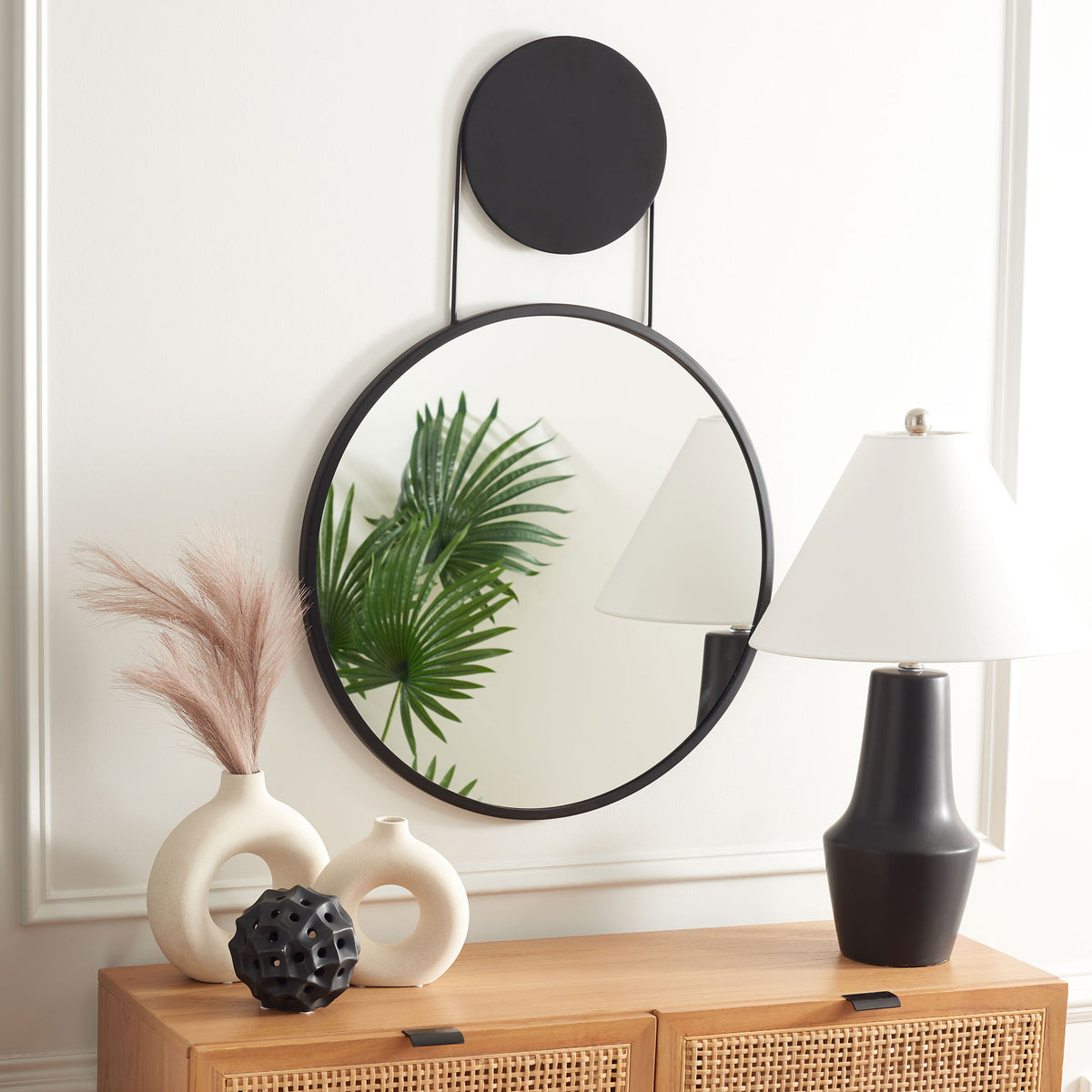 A round black-framed mirror and matching circular accent add graphic contrast above a wood console.