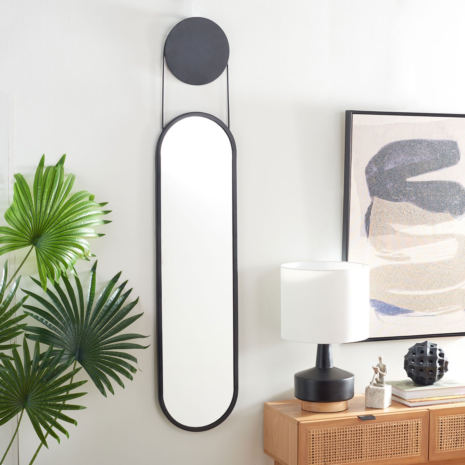 A slim, black-framed mirror adds modern contrast to a bright room with lush greenery and warm wood. || MRR3072A || front_room