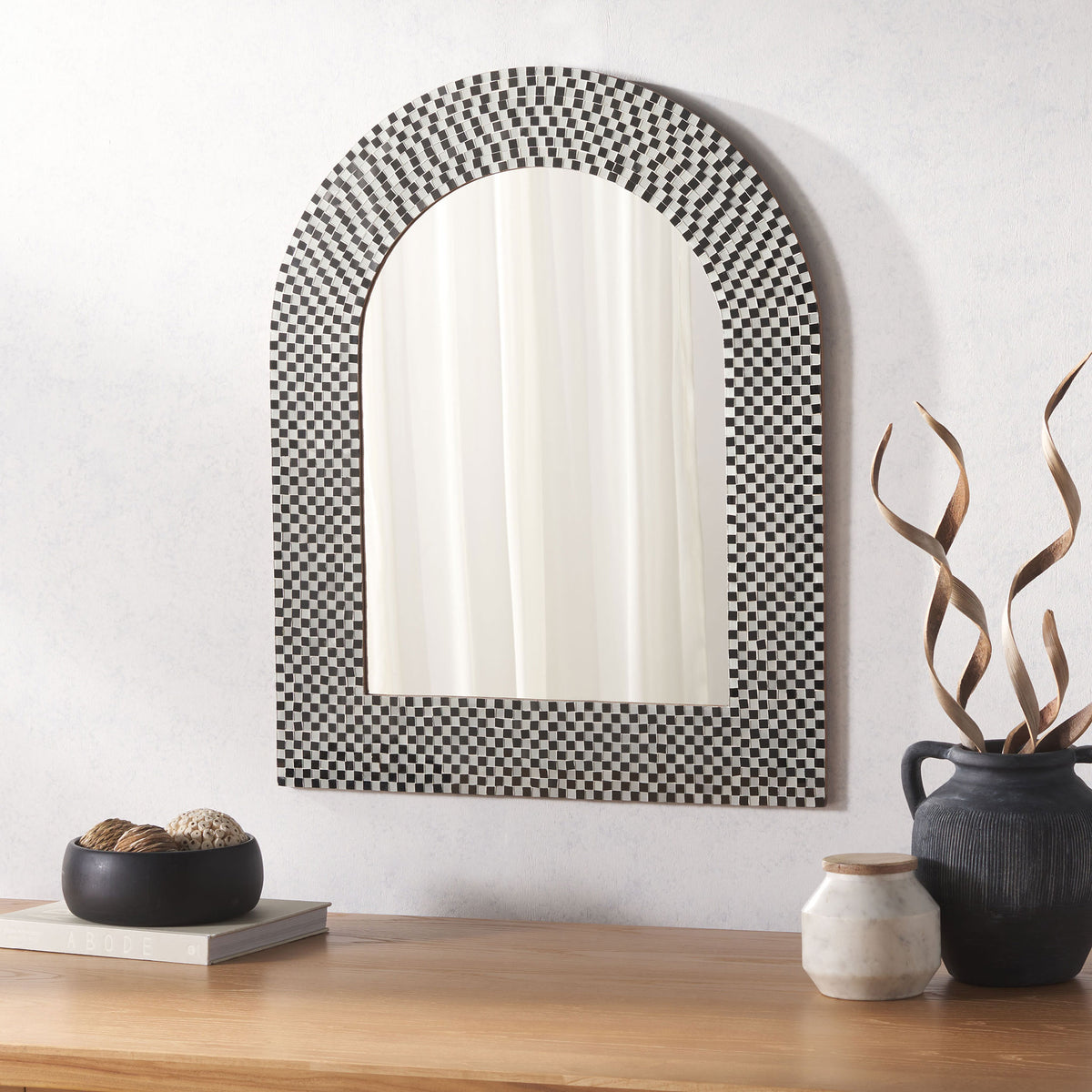 Black and white mosaic arch mirror brings geometric contrast above a wood console.