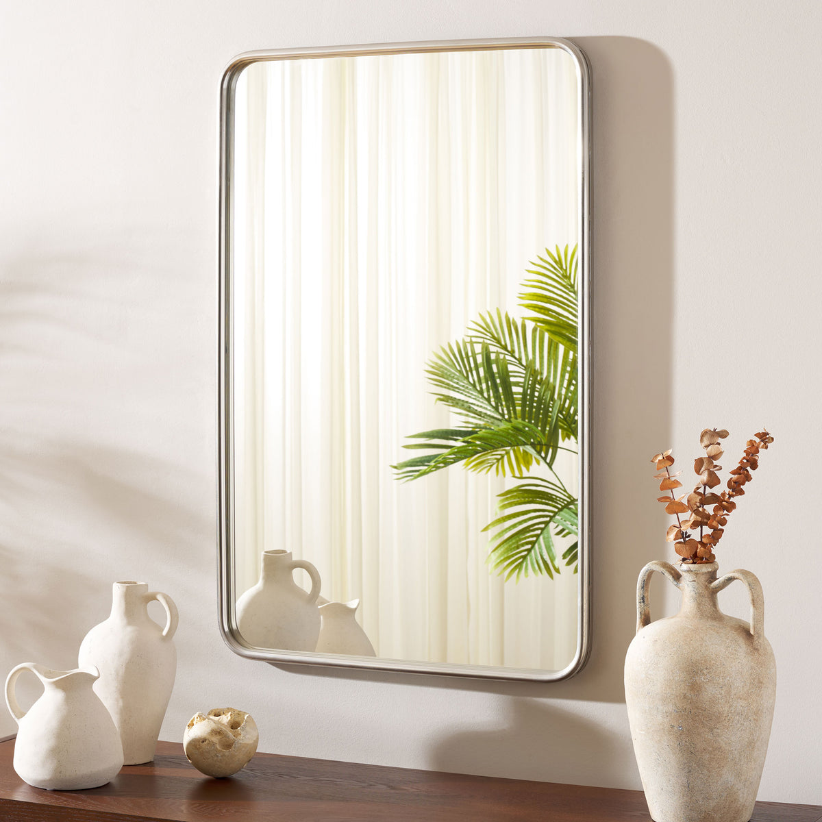 Chrome-framed wall mirror reflects greenery above a display of sculptural vases || MRR4006A || front_room