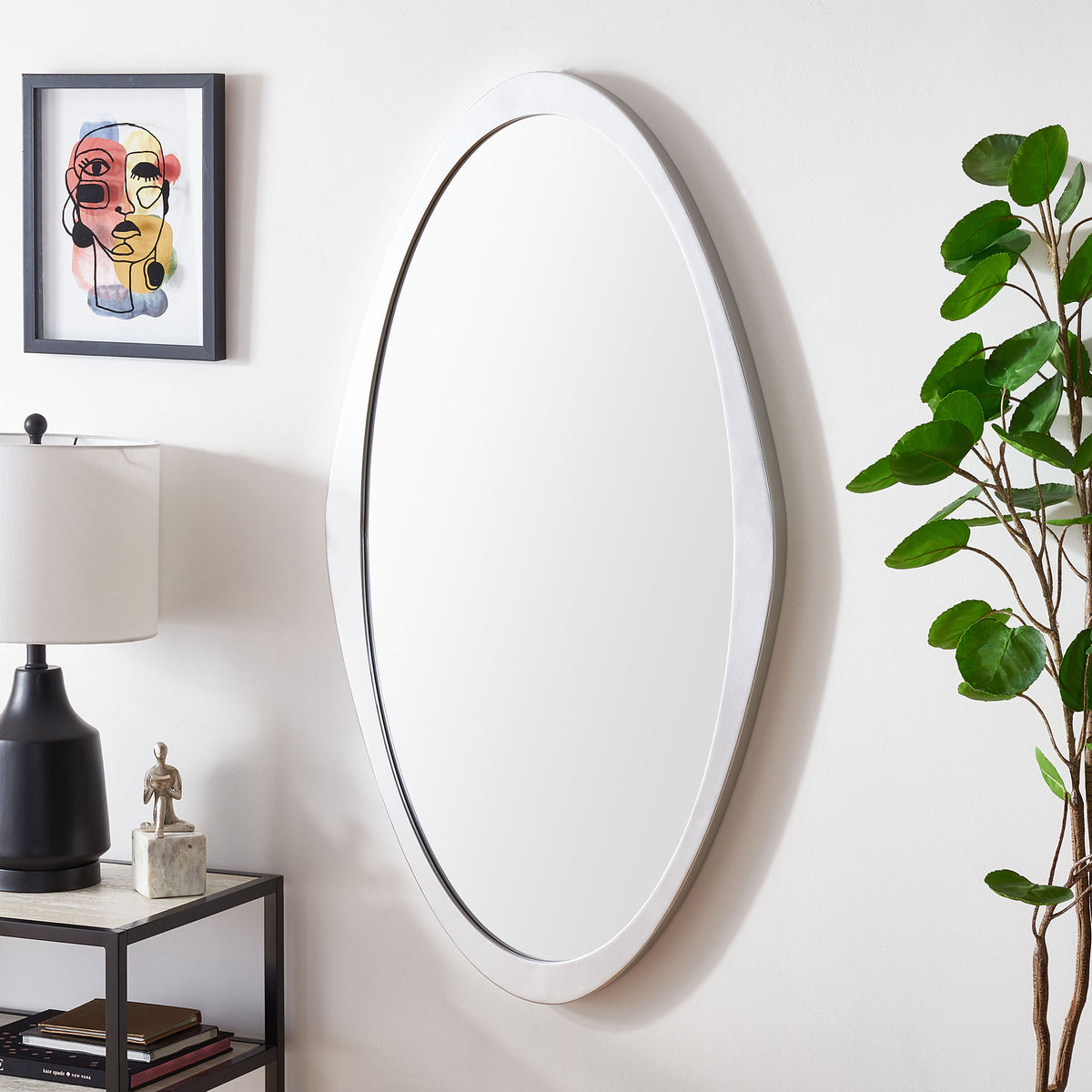 A tall silver-framed mirror adds a sleek accent beside a table lamp and leafy greenery. || MRR8002A || front_angle_room