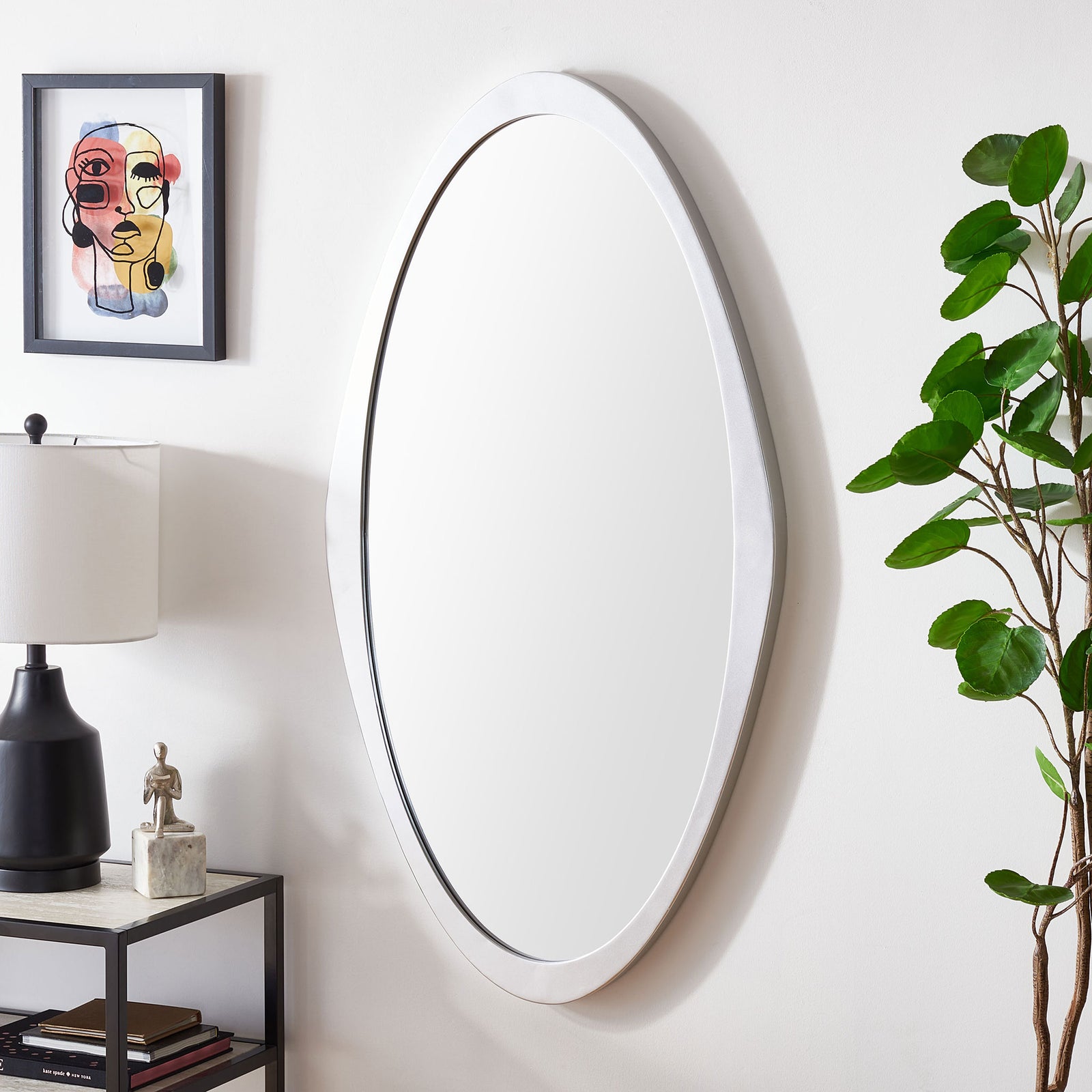 A tall silver-framed mirror adds a sleek accent beside a table lamp and leafy greenery. || MRR8002A || front_angle_room