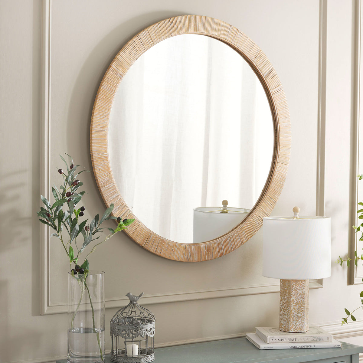 A round wall mirror with a warm, woven frame adds inviting texture above a console table. || MRR9001A || front_angle_room
