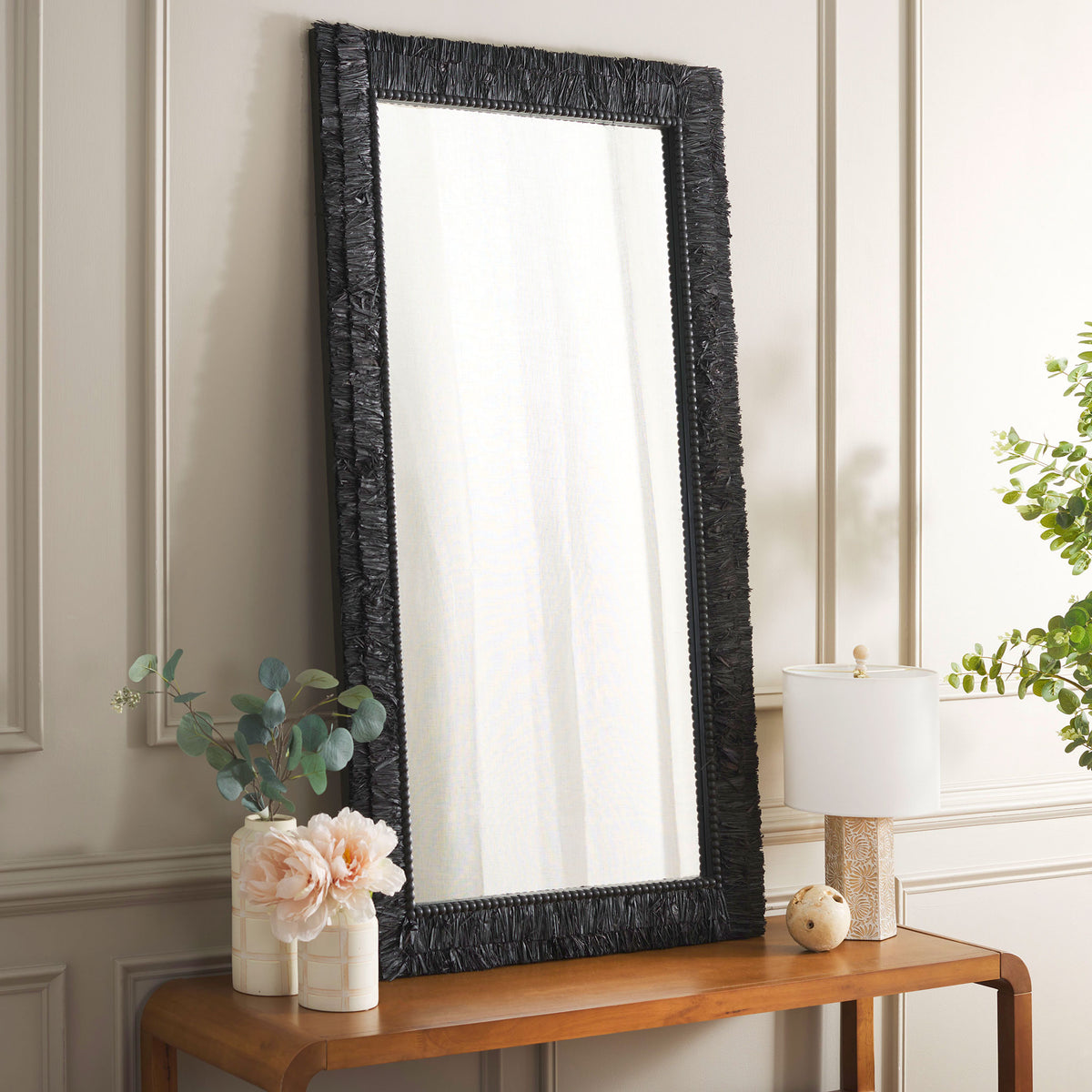 The tall black mirror adds striking texture atop a warm wood console in a neutral room. || MRR9003B || front_angle_room