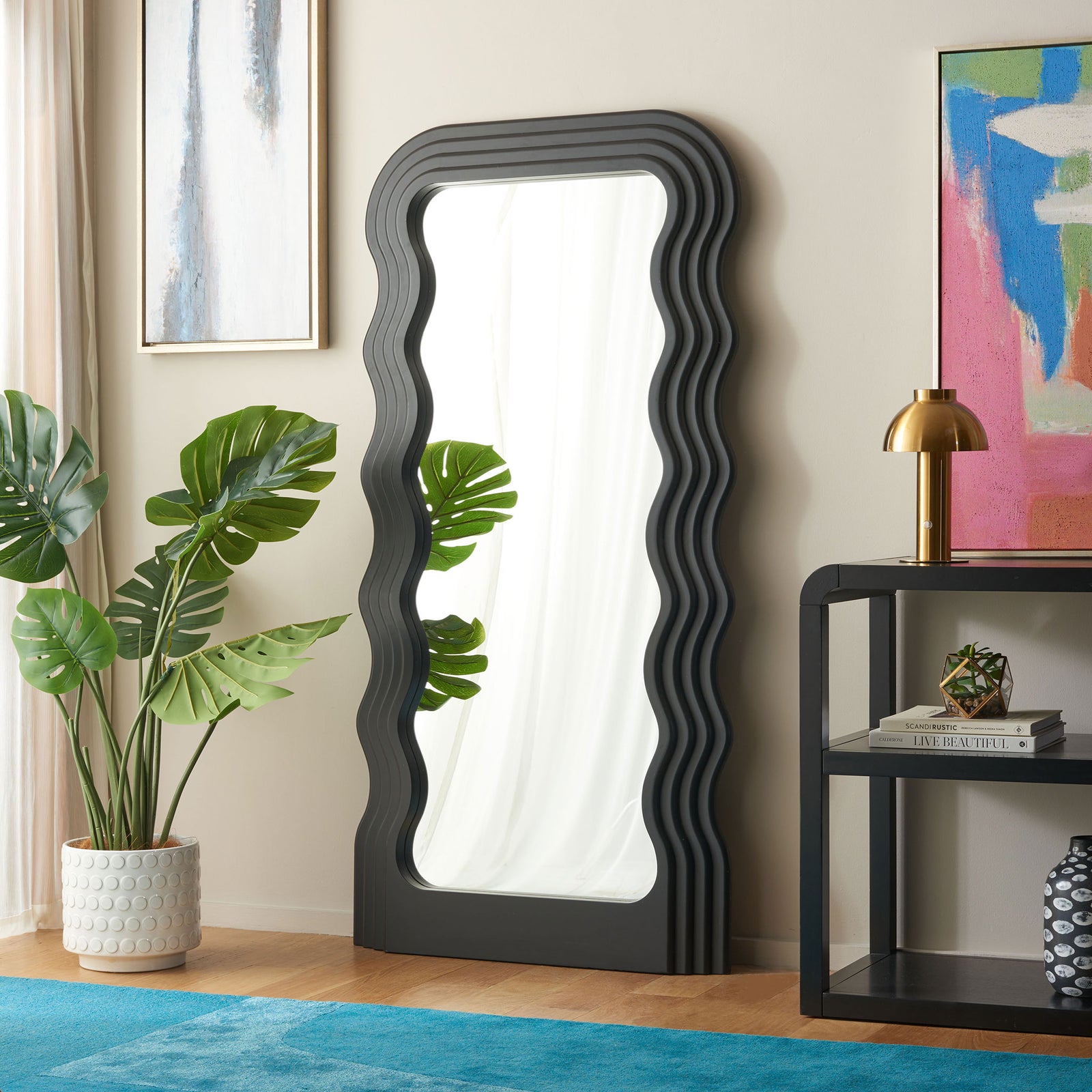 Sculptural black mirror adds flowing curves beside greenery and living room furnishings || MRR9006A || front_angle_room