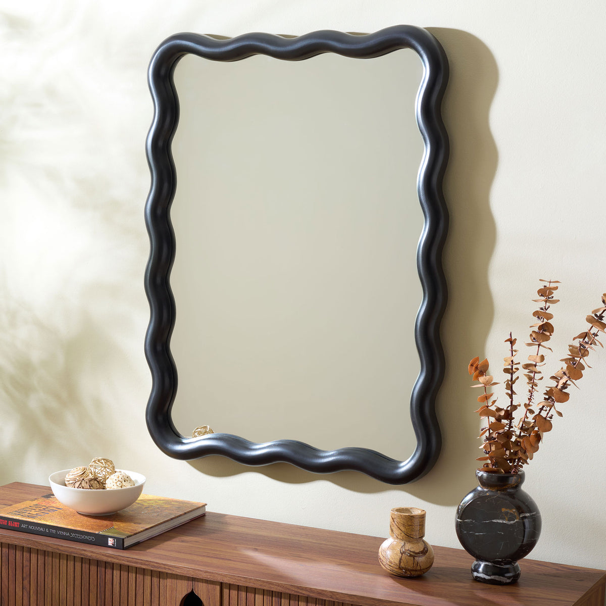 Wavy black wall mirror adds striking contrast above a wood console || MRR9007B || front_angle_room