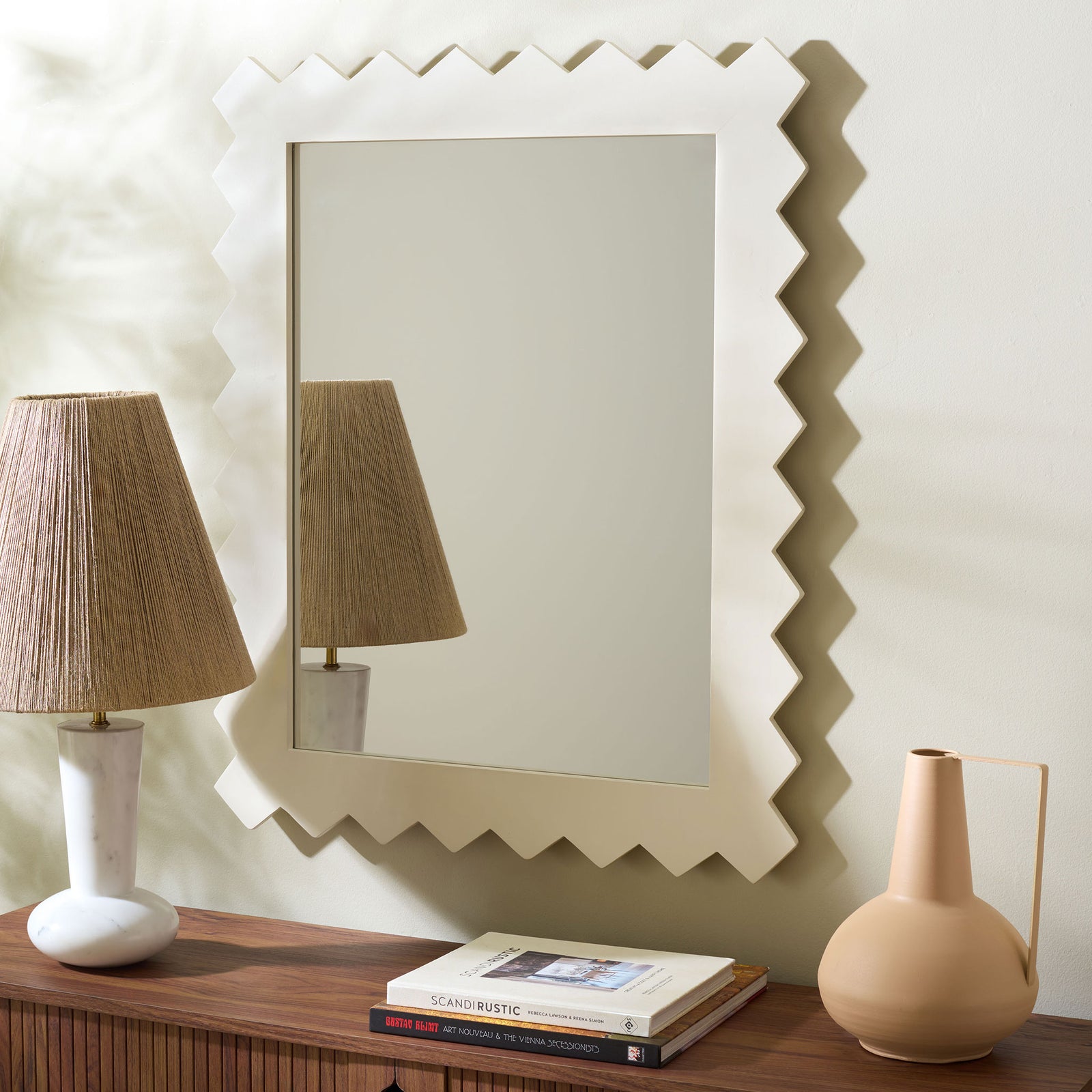 White zigzag-framed mirror hangs above a wood console and reflects a textured lamp. || MRR9010B || front_room