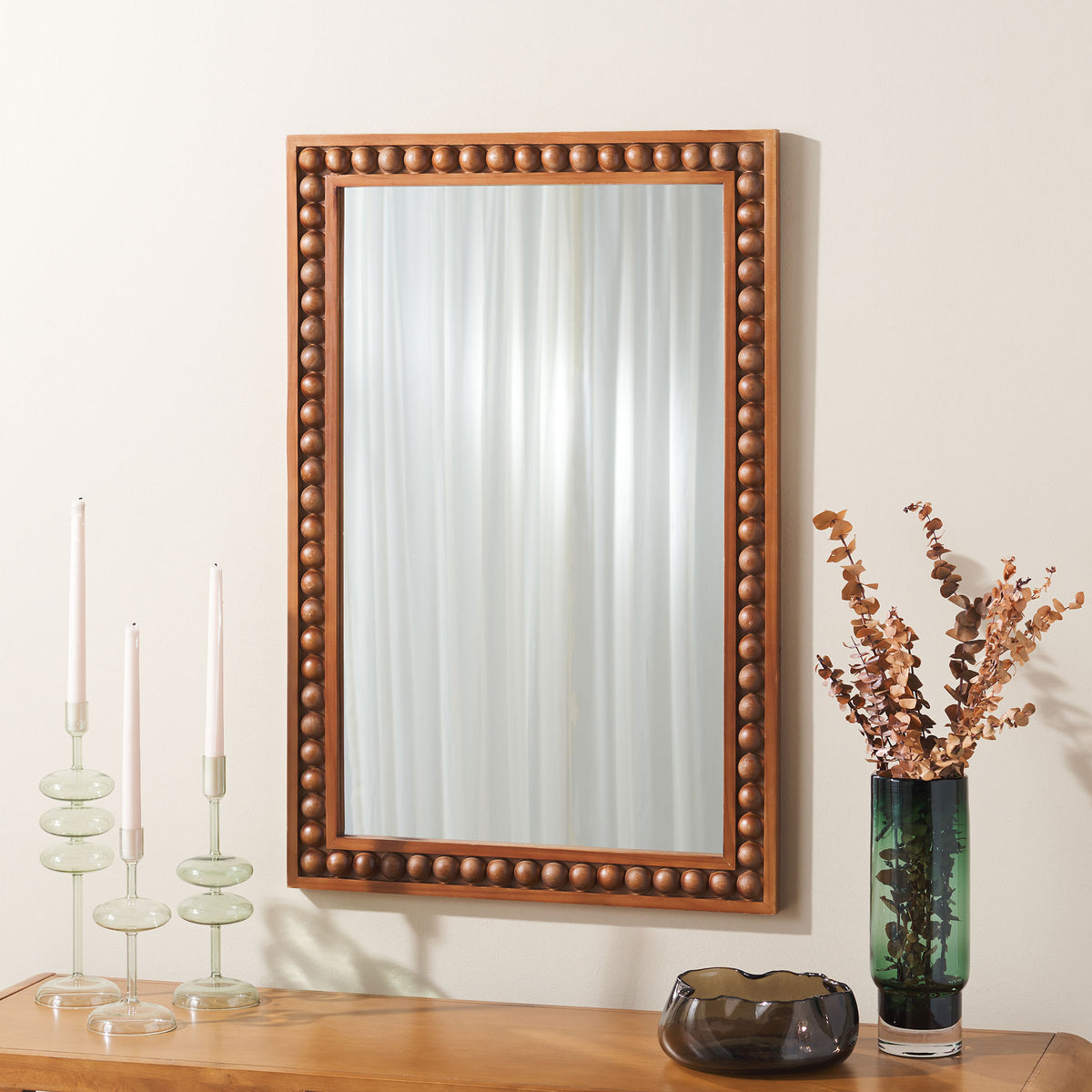 A beaded wood frame makes this wall mirror an inviting focal point above a wood console.