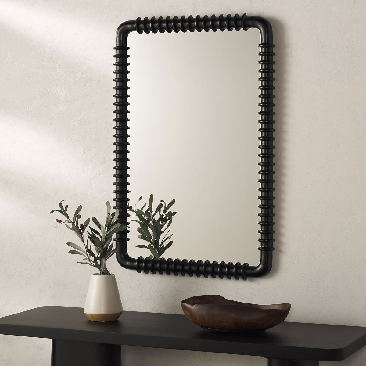 A tall black mirror with raised rings complements a dark console and simple greenery. || MRR9024A || front_room