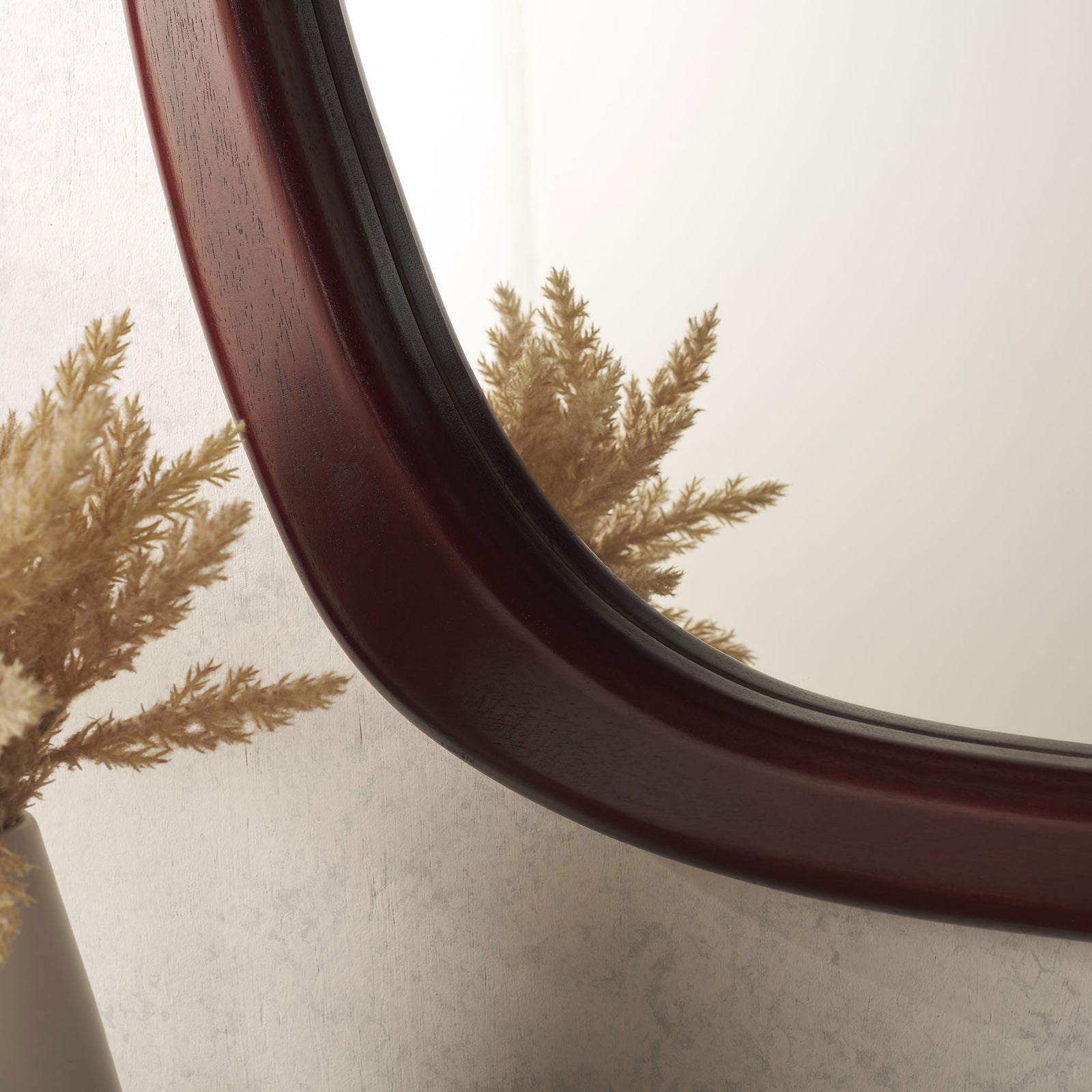 A glossy, deep reddish-brown wood frame sweeps around the mirror's softly curved corner. || MRR9025A || detail_room