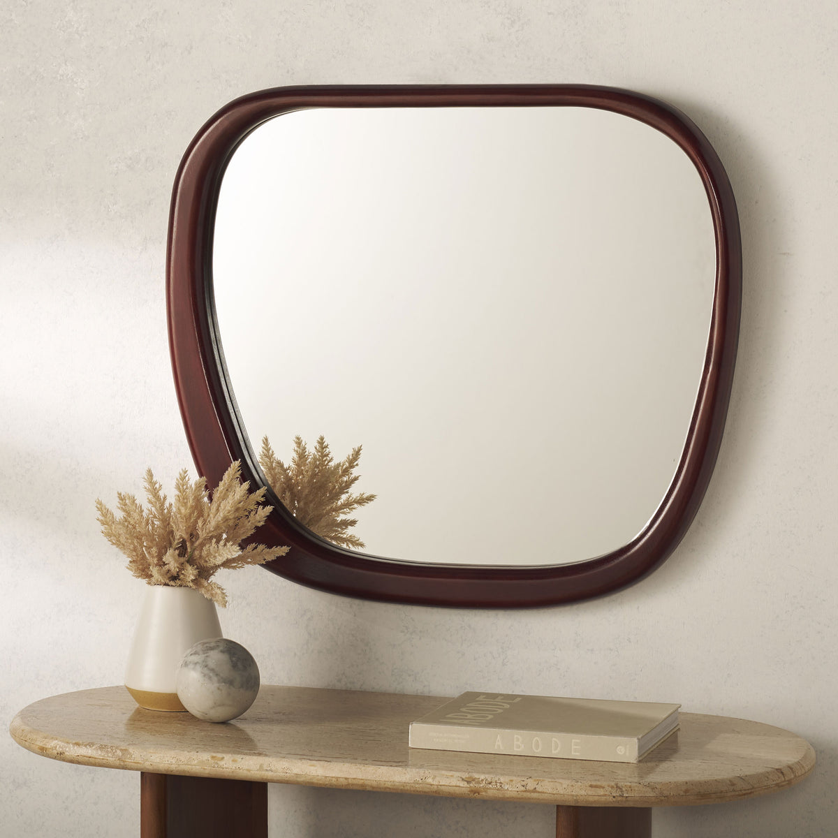A softly rounded mirror in a deep reddish-brown wood frame adds warmth above a console table. || MRR9025A || front_room