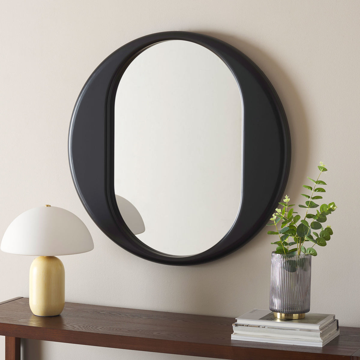 Sculptural black wall mirror adds a striking round silhouette above a wood console || MRR9034A || front_room