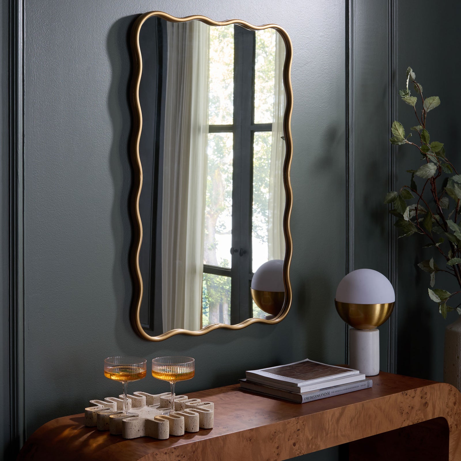 A wavy gold-framed mirror brightens a dark wall above a warm wood console || MRR9036A || front_room