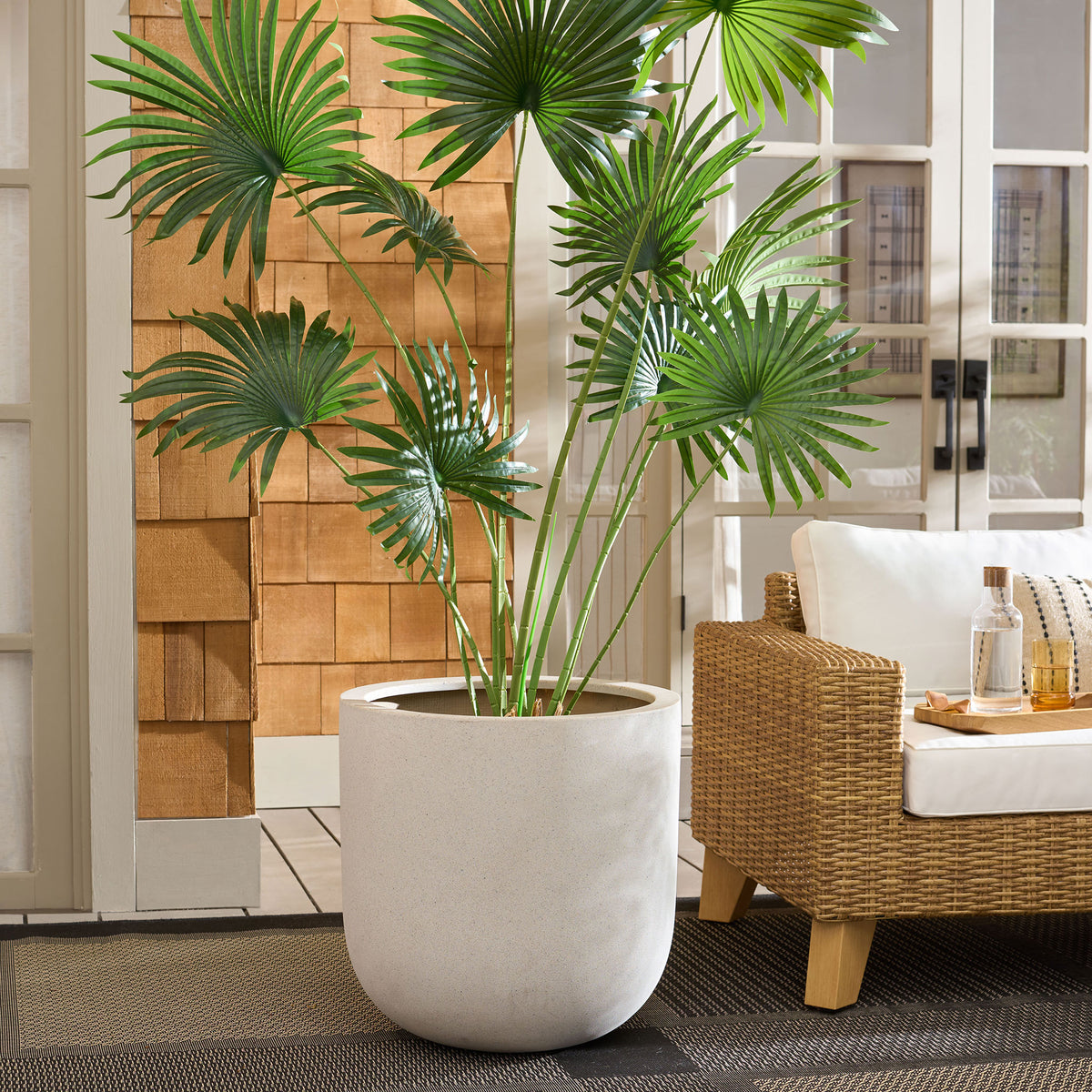 Wide beige planter holds fan palms alongside a woven outdoor lounge chair || PAT1401B || front_room