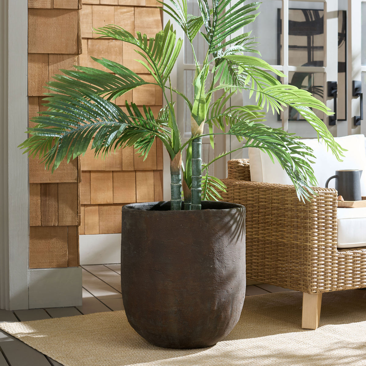 A large brown planter grounds leafy greenery in a warm patio setting. || PAT1405A || front_room