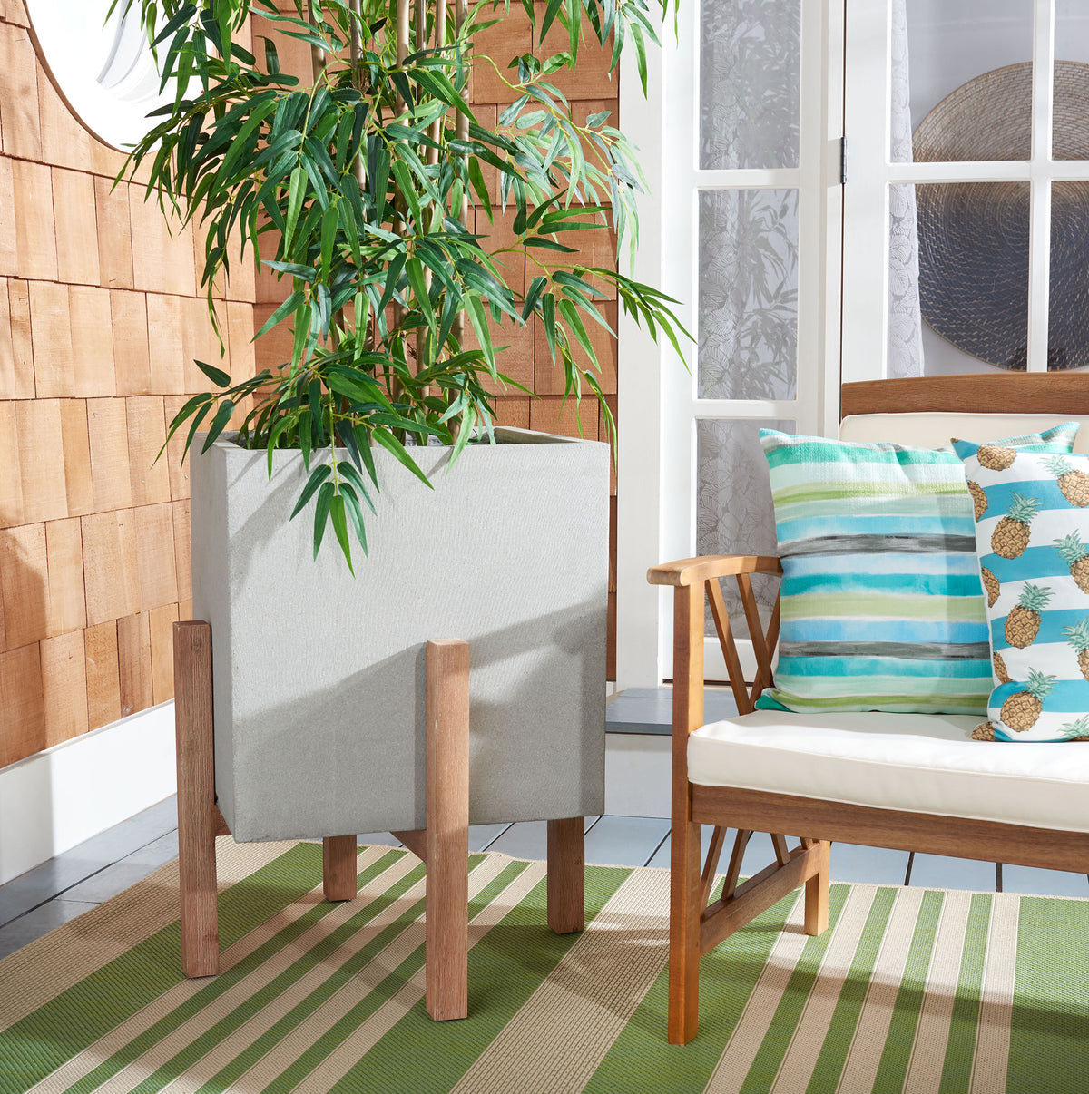 A tall leafy plant flourishes in the large light gray cube planter on a natural wood stand. || PAT1513B || front_angle_room