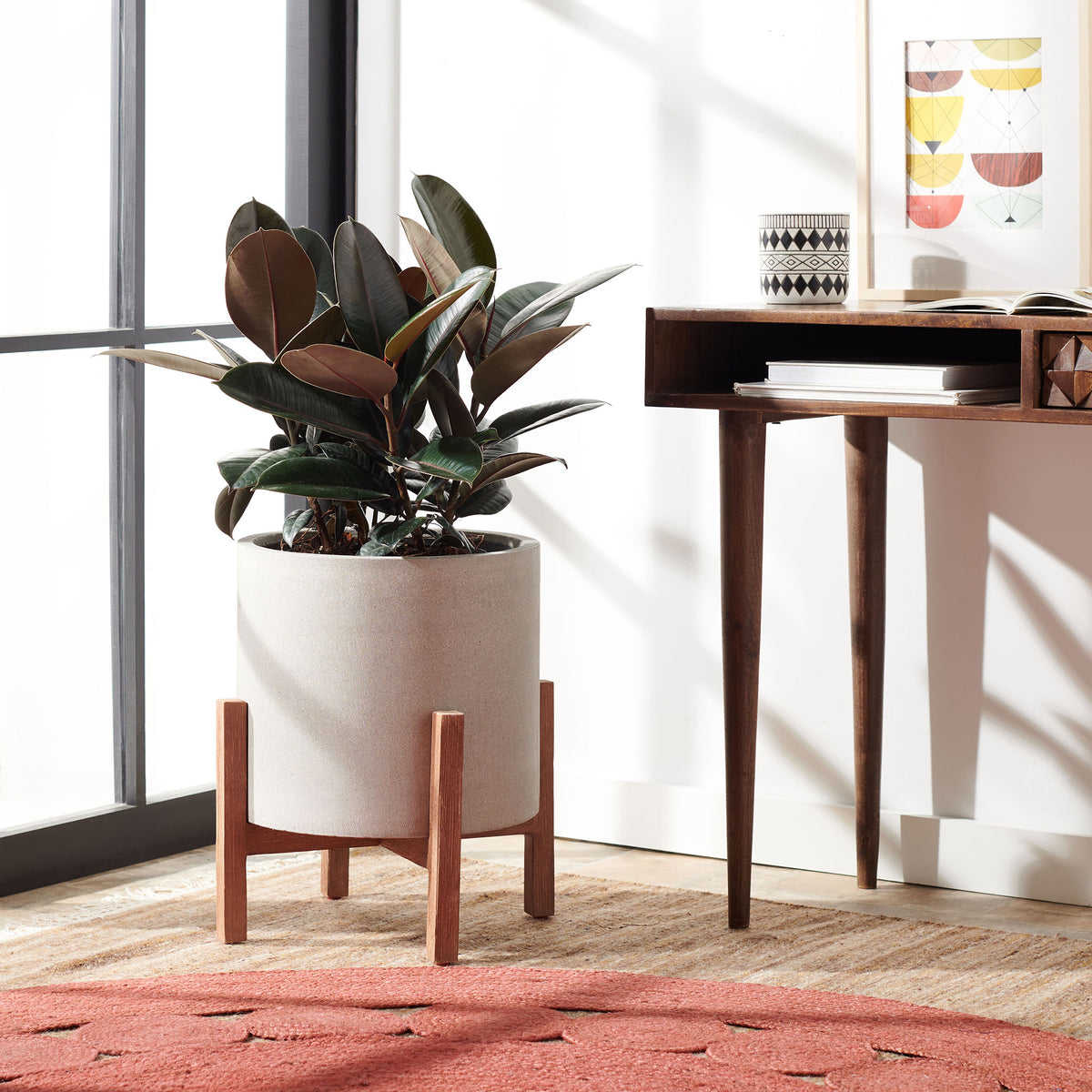 Leafy greenery fills a pale gray planter raised on warm wood legs beside a desk. || PAT1514B || front_room