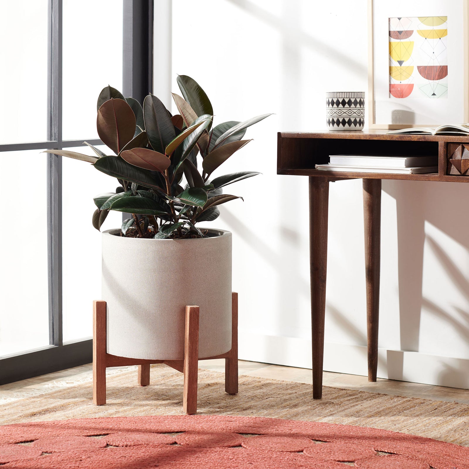 Leafy greenery fills a pale gray planter raised on warm wood legs beside a desk. || PAT1514B || front_room