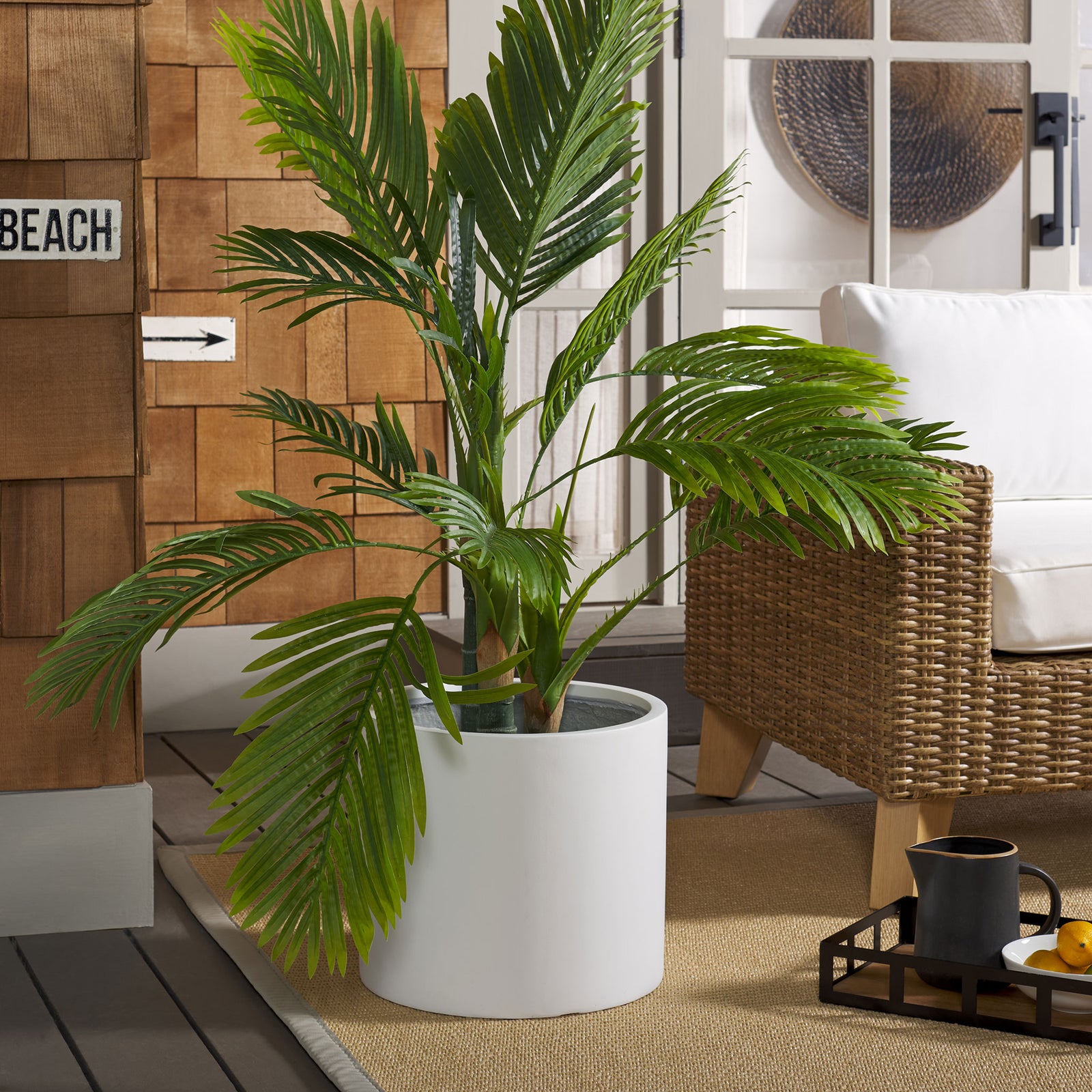 A crisp white planter highlights lush palm foliage beside woven patio seating || PAT1516C || front_angle_room