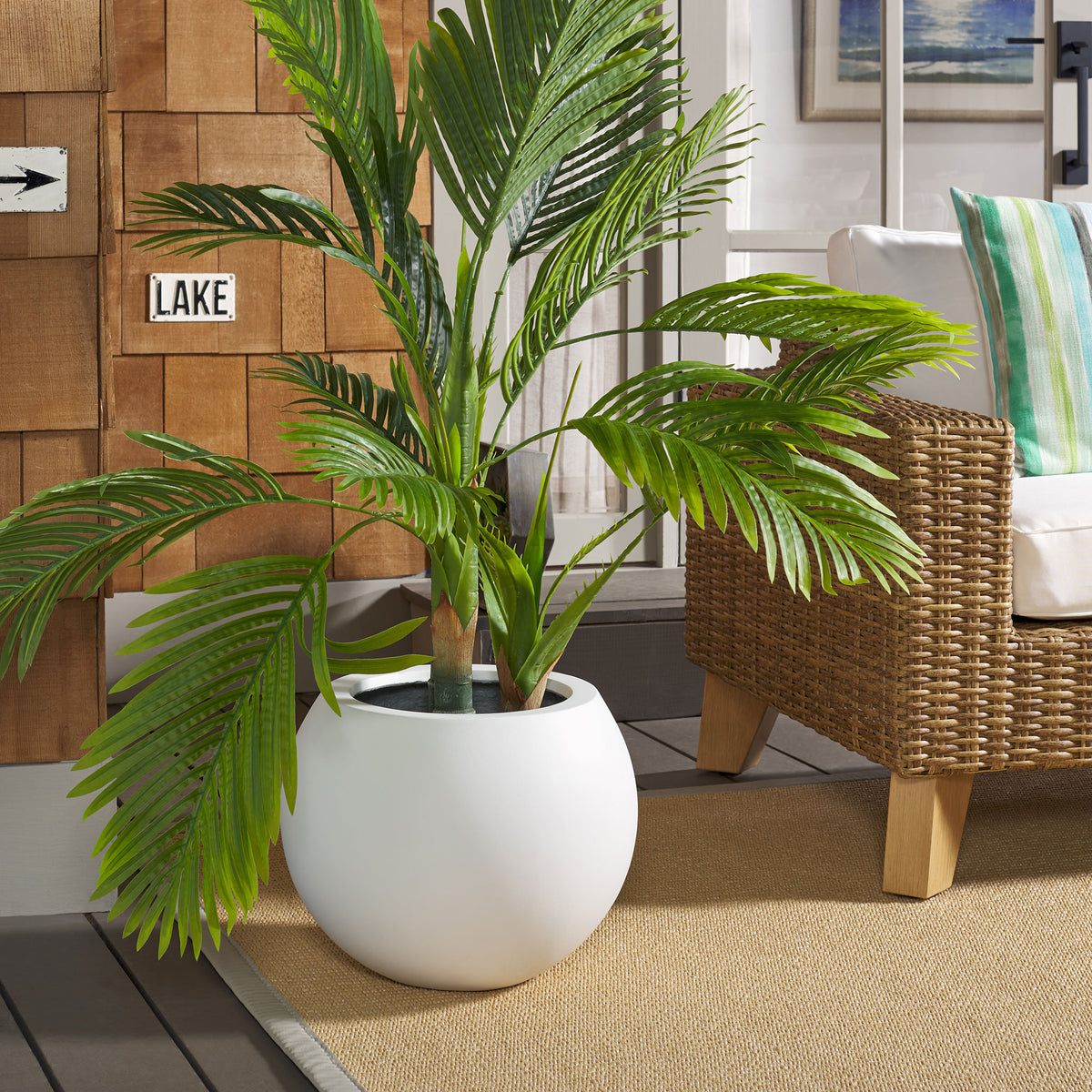 A crisp white orb planter showcases tall palm leaves alongside woven patio seating. || PAT1518C || front_room
