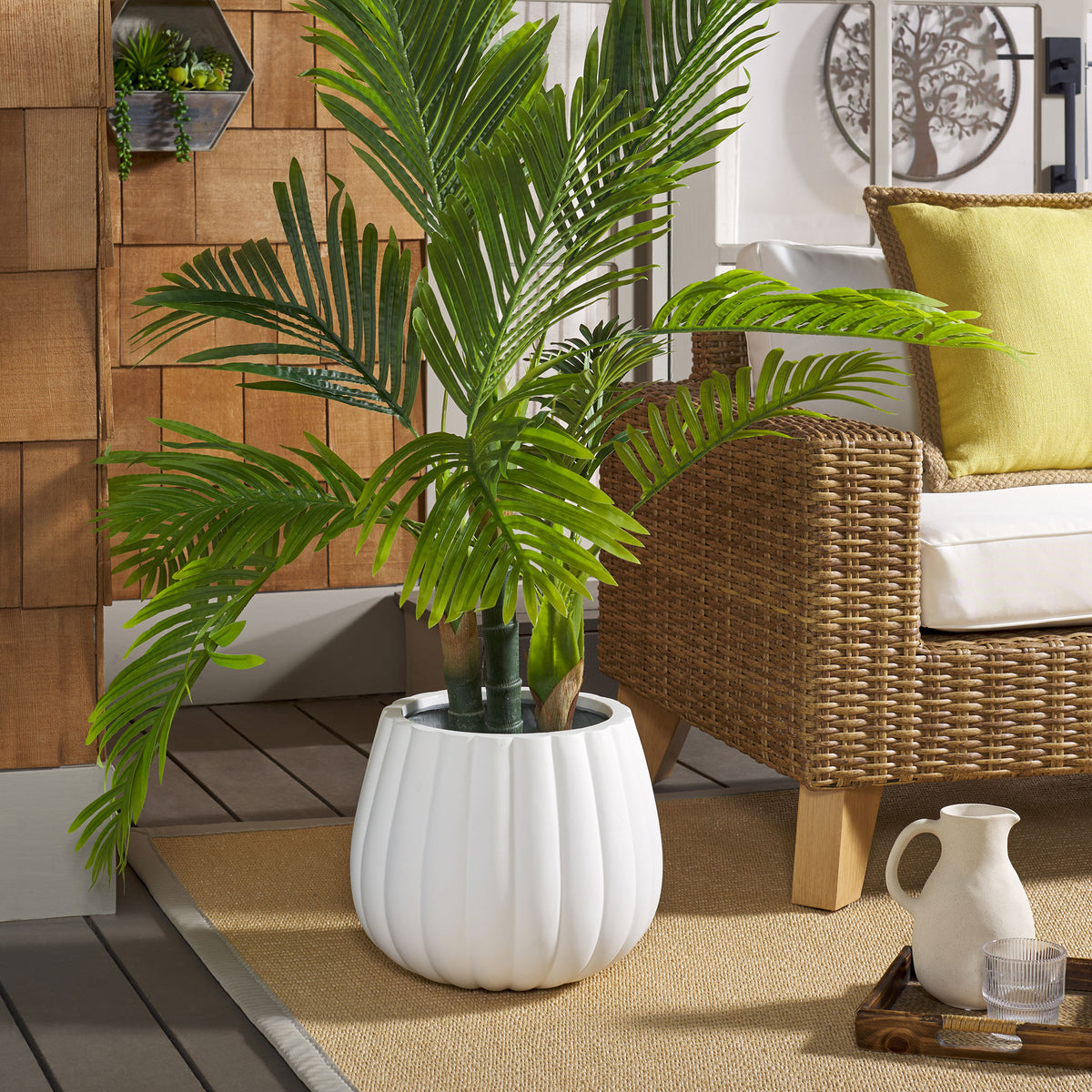 White fluted planter holds a leafy palm beside wicker patio seating