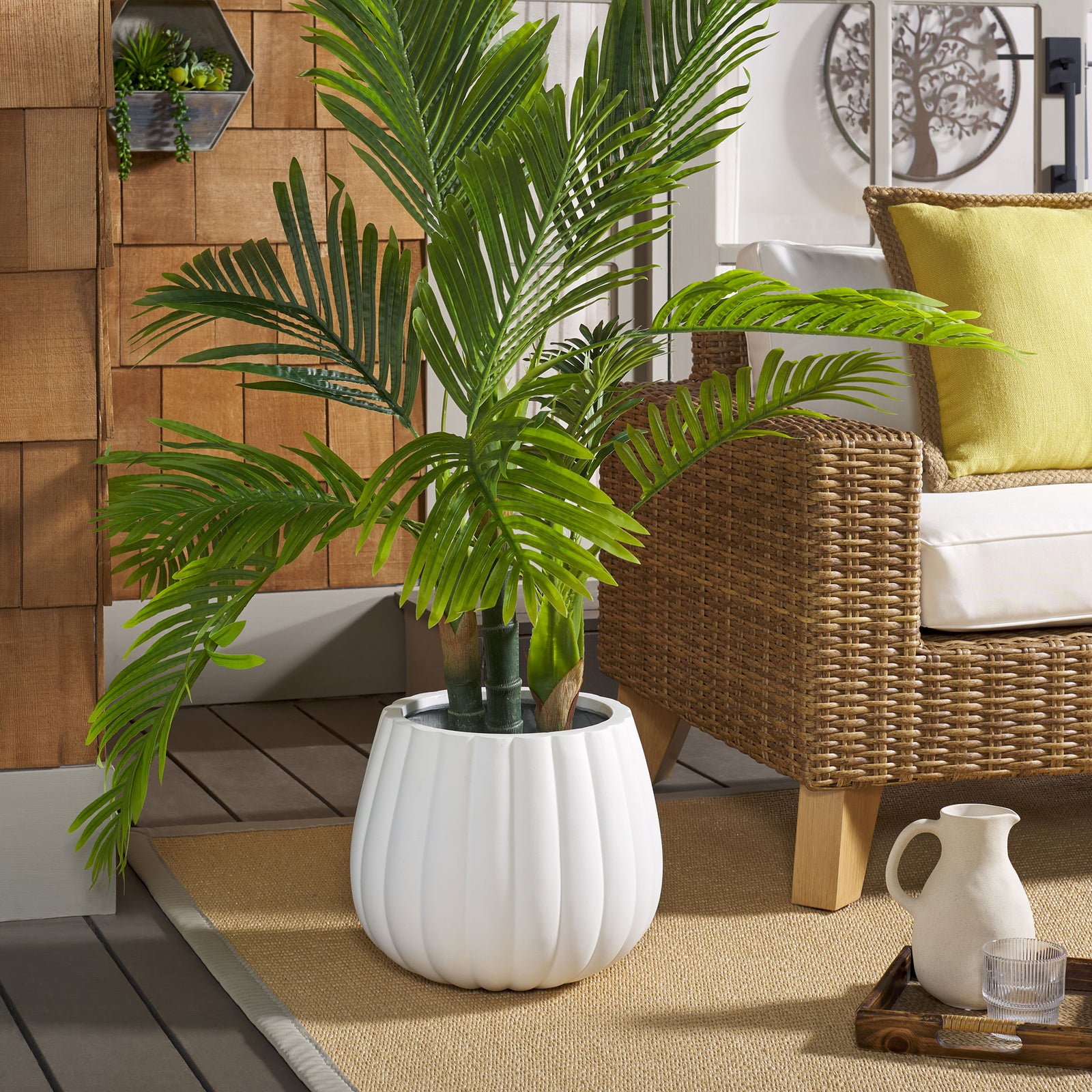 White fluted planter holds a leafy palm beside wicker patio seating || PAT1522C || front_room