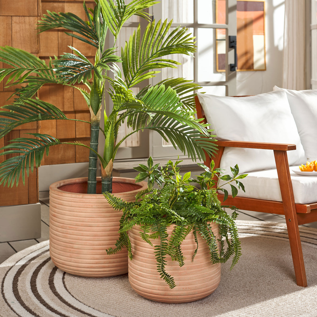 Two terracotta ribbed planters cradle leafy plants beside a welcoming cushioned seat