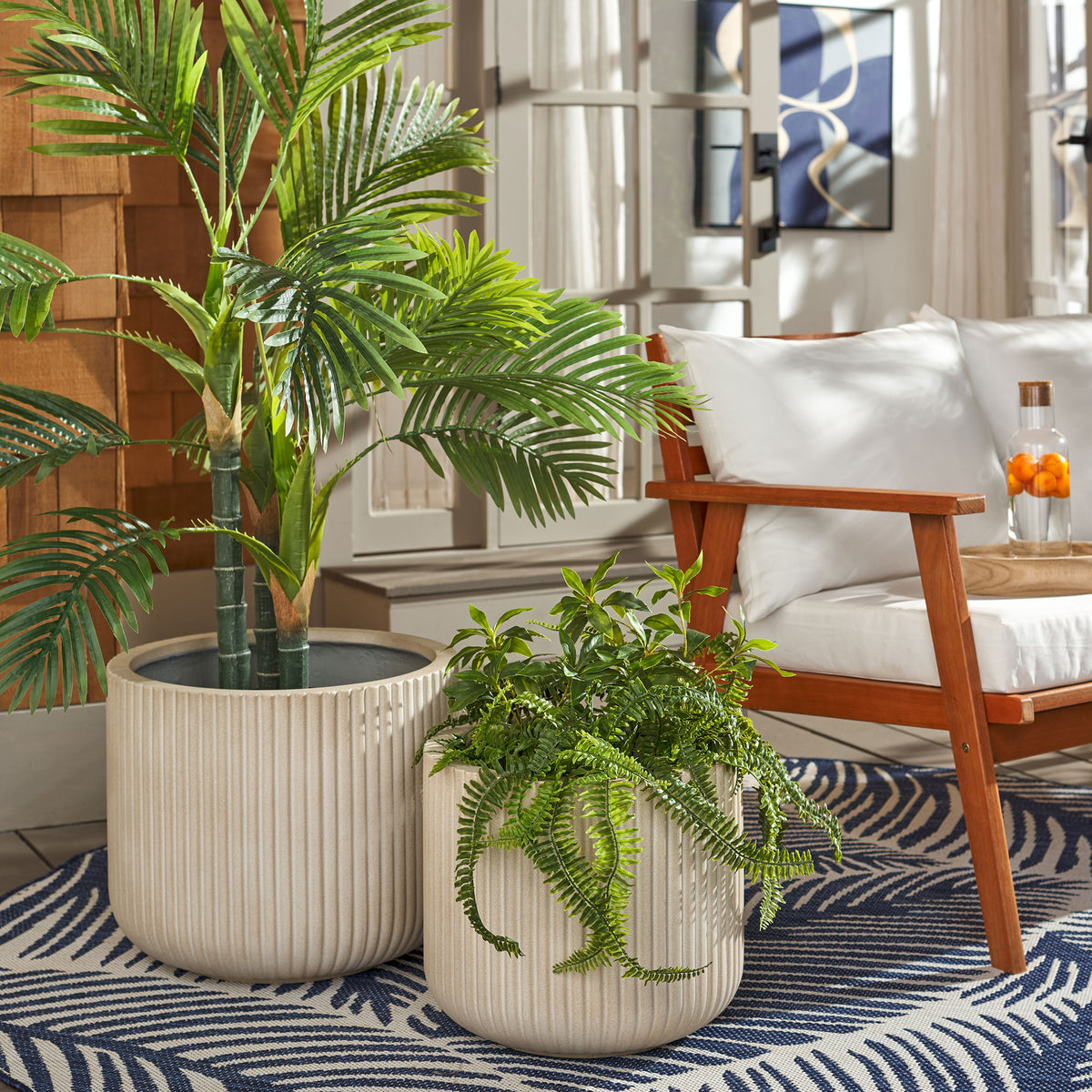 Beige fluted planters give a palm and trailing fern a coordinated home beside a cushioned chair. || PAT1532B-SET2 || front_angle_room