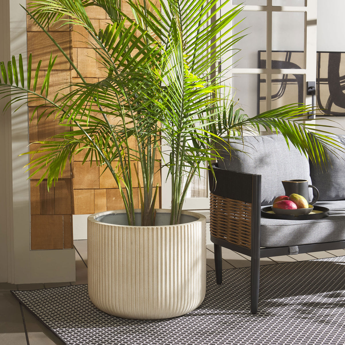 A ribbed beige planter holds a tall palm beside a patio chair, warming the lounge setting.