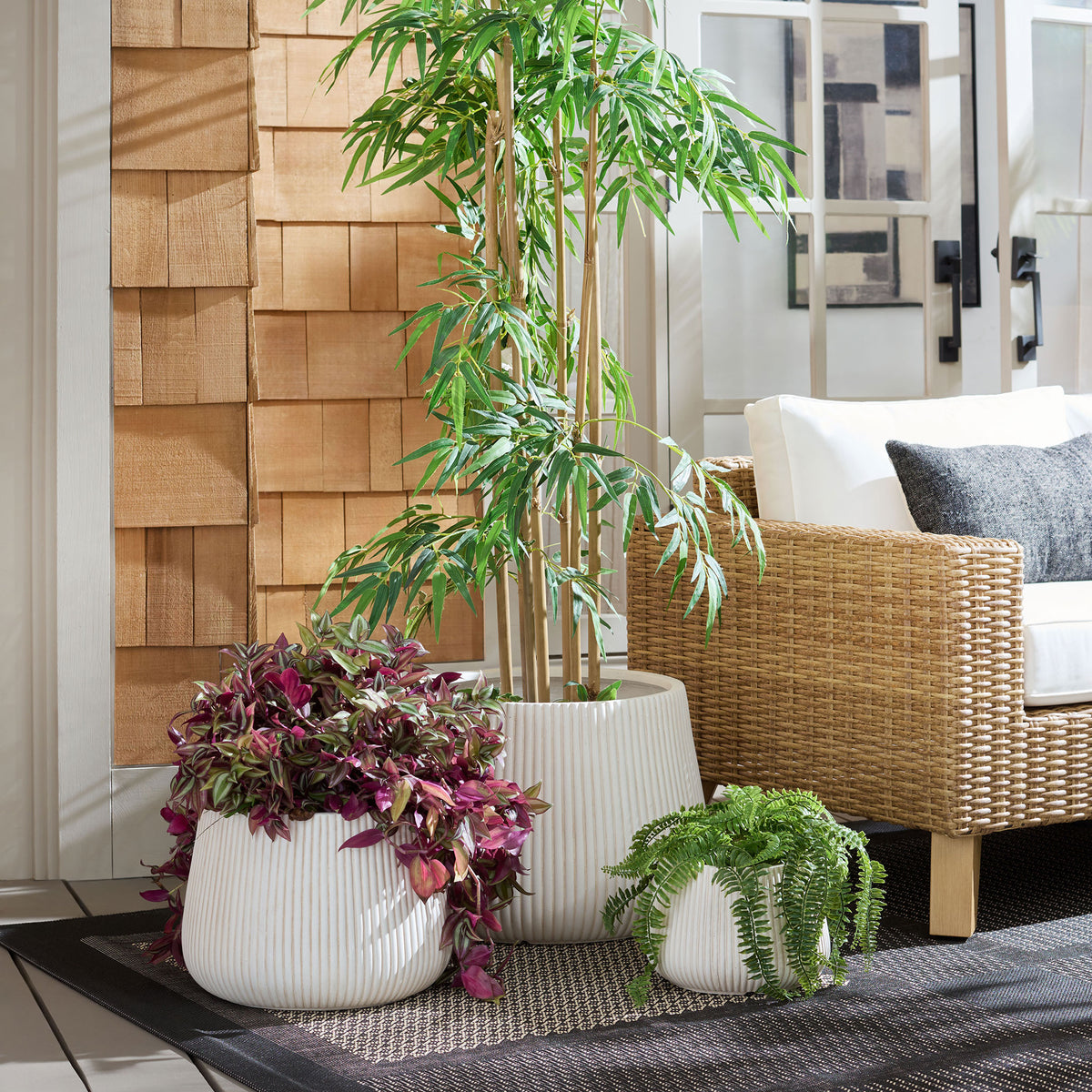 Beige ribbed planters hold a leafy tree, colorful foliage, and a fern beside a woven lounge chair || PAT4601B-SET3 || front_room