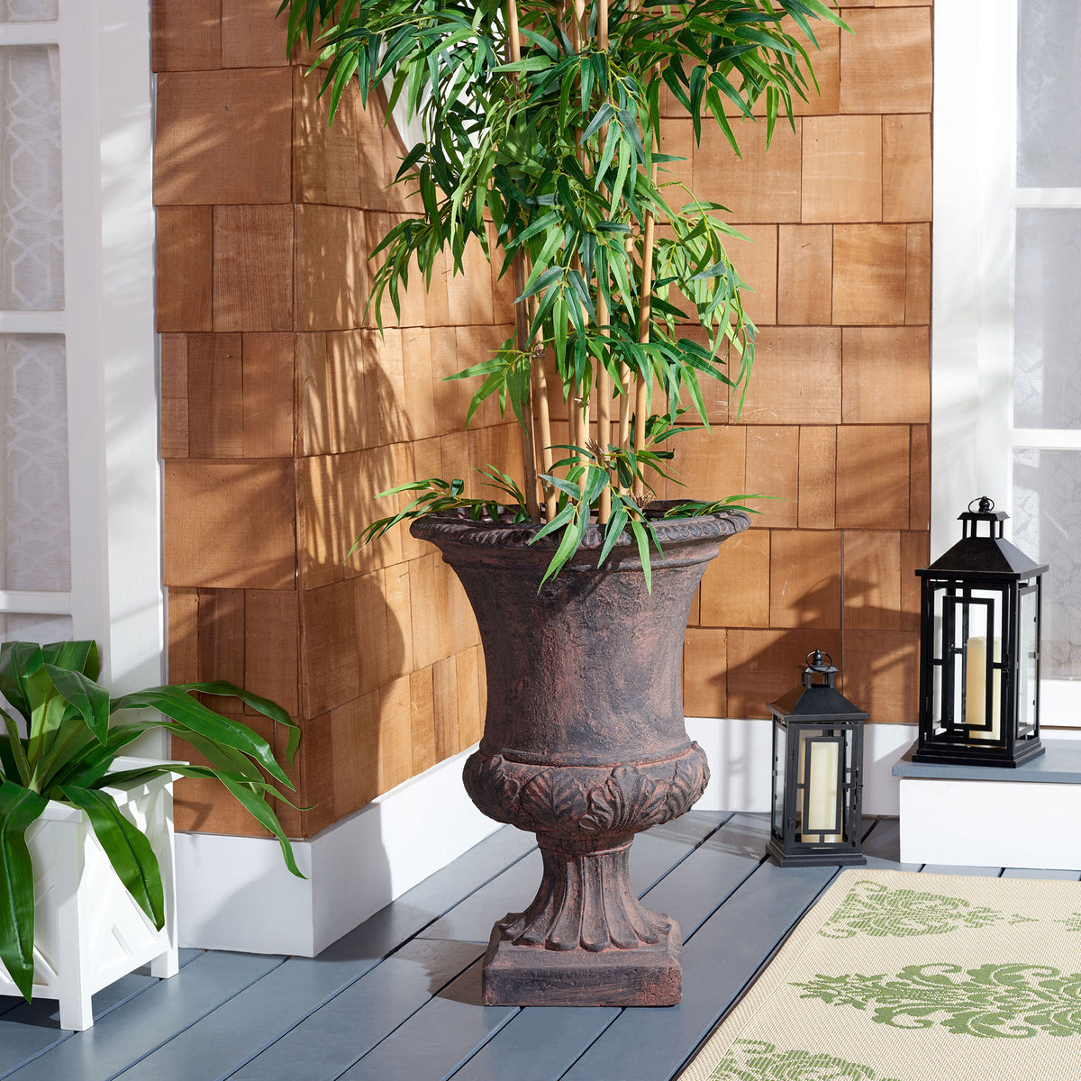 An antiqued brown urn planter supports tall greenery on a sheltered porch. || PAT5038B || front_room