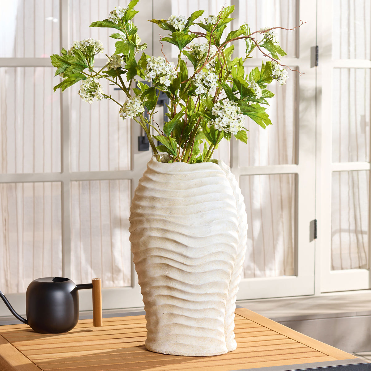 White blossoms and greenery brighten a ribbed off-white planter on a slatted tabletop