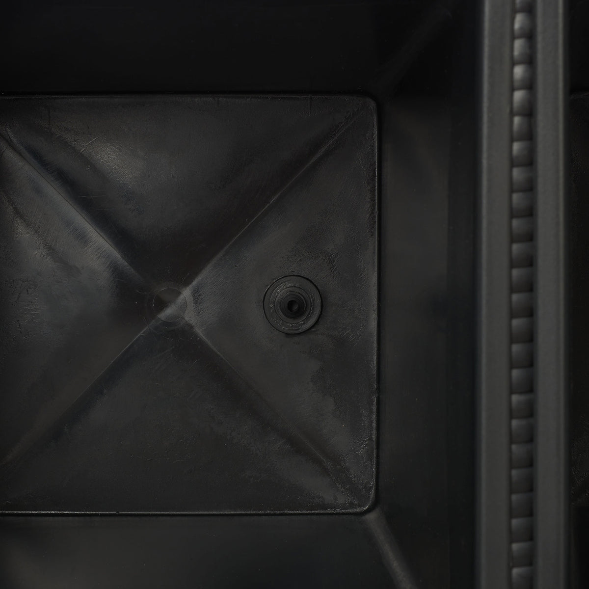 A circular drain opening is molded into the base of a black planting bin. || PAT7705A || detail_studio