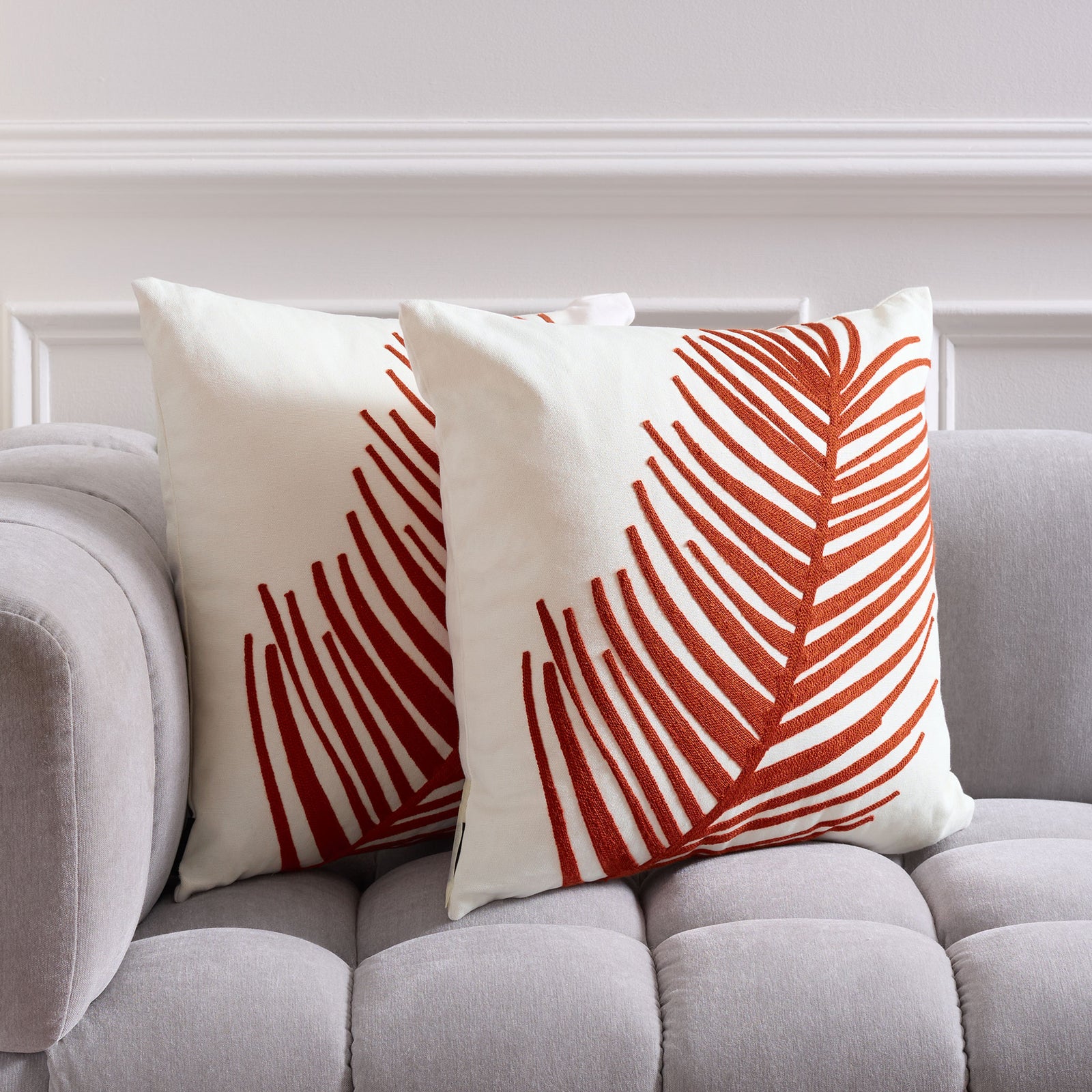 A pair of sienna-orange palm frond pillows brightens a soft gray sofa || PIL861A-1818-SET2 || front_multi_room
