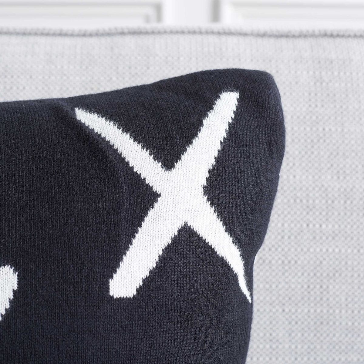 Black pillow corner shows soft knit texture and sharp white X pattern. || PLS404A-1818-SET2 || detail_room