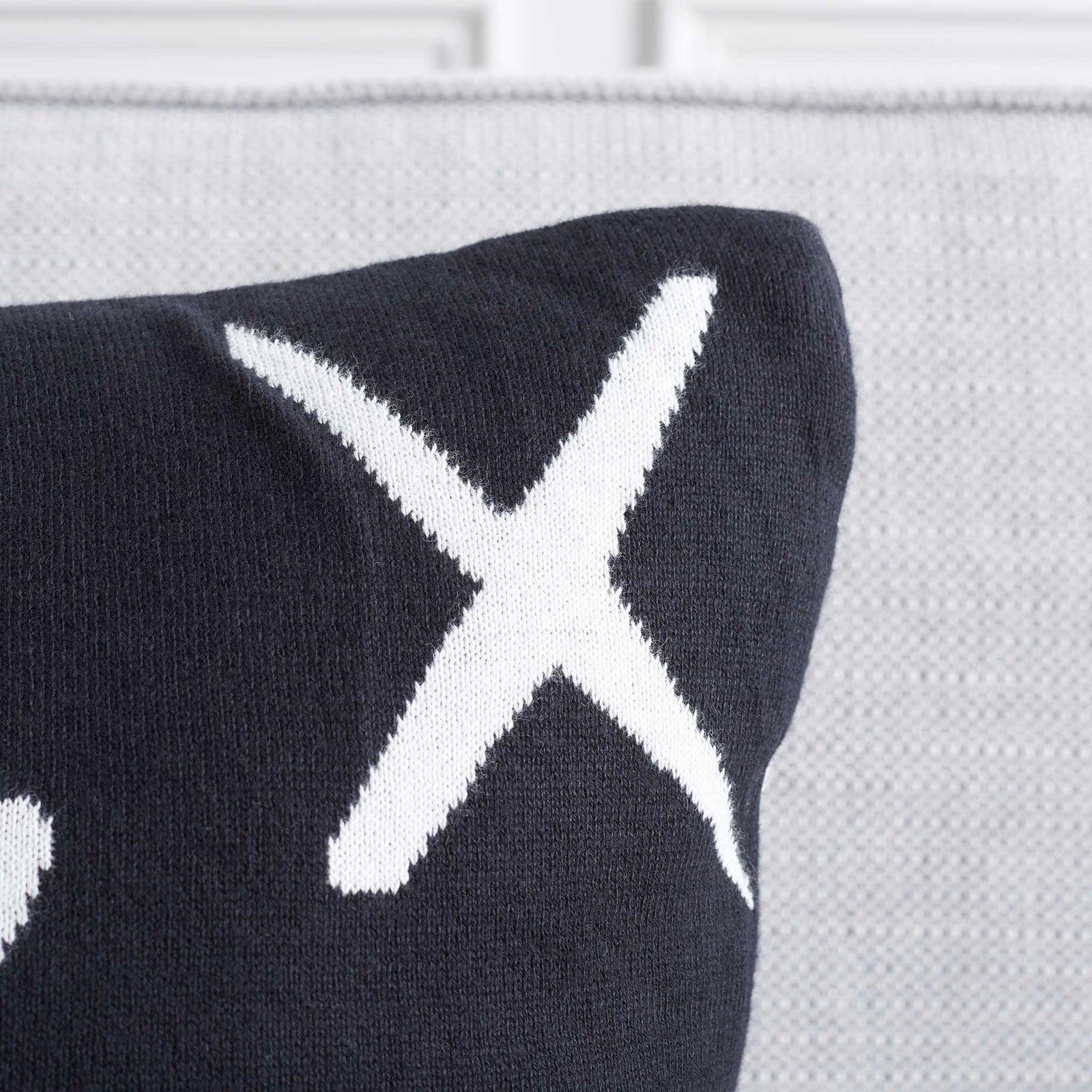 Black pillow corner shows soft knit texture and sharp white X pattern. || PLS404A-1818-SET2 || detail_room
