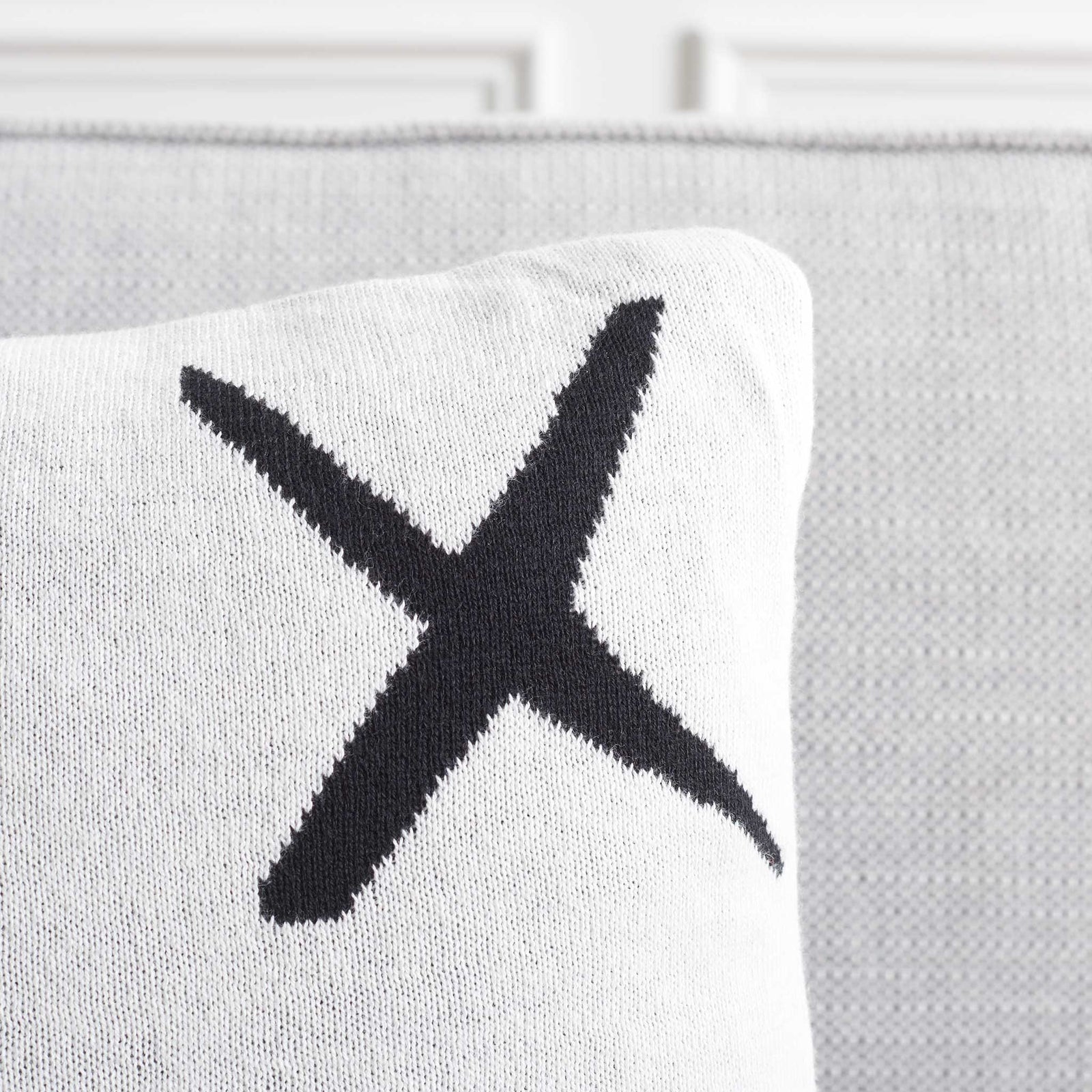 Ivory pillow corner shows soft knit texture and bold black X detail. || PLS404A-1818-SET2 || detail_room