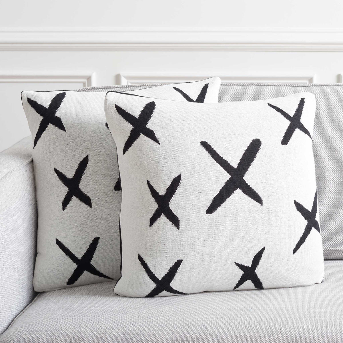 Pair of ivory X-pattern pillows bringing bold contrast to a modern sofa. || PLS404A-1818-SET2 || back_angle_multi_room