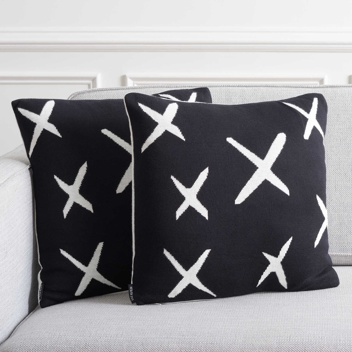 Pair of black X-pattern pillows adding graphic contrast on a light sofa. || PLS404A-1818-SET2 || front_angle_multi_room