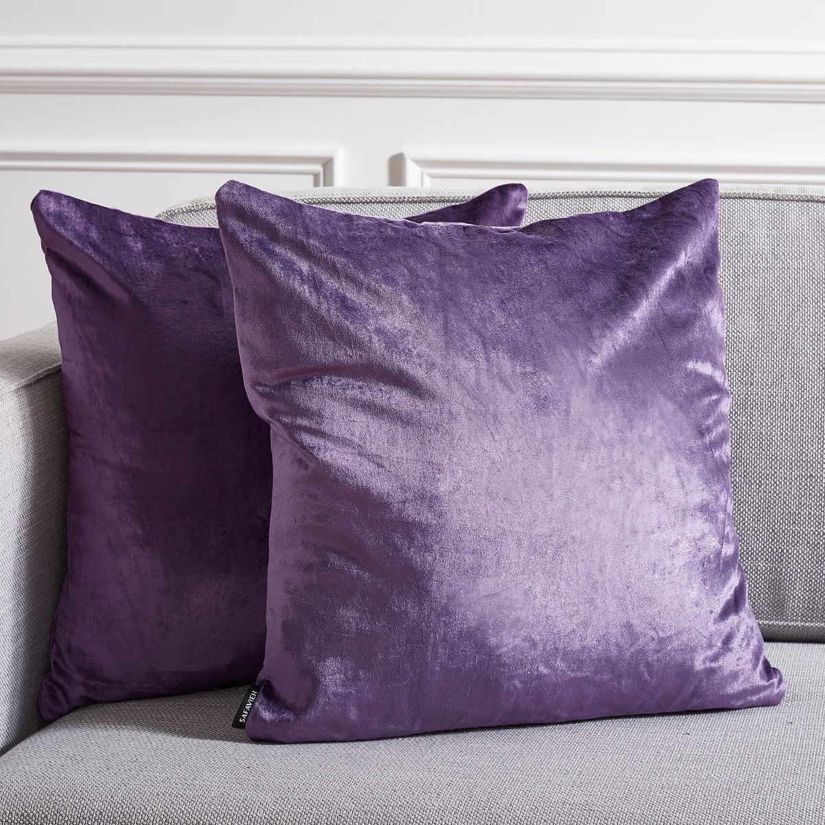 Two rich purple accent pillows warm a neutral sofa with luminous, velvety texture.