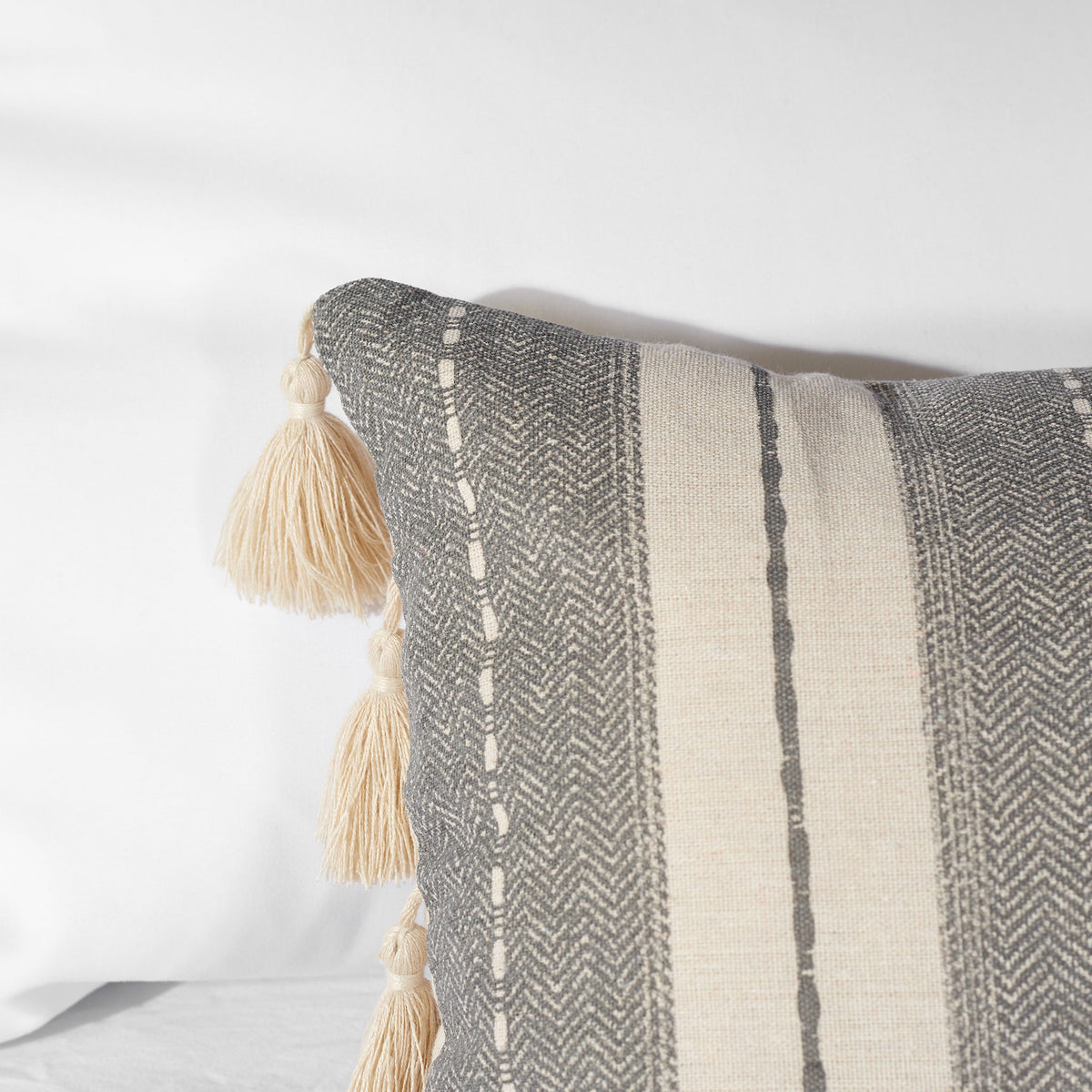 Chevron-textured gray stripes and cream tassels add dimension to the beige pillow || PLS7165A-1236 || detail_room