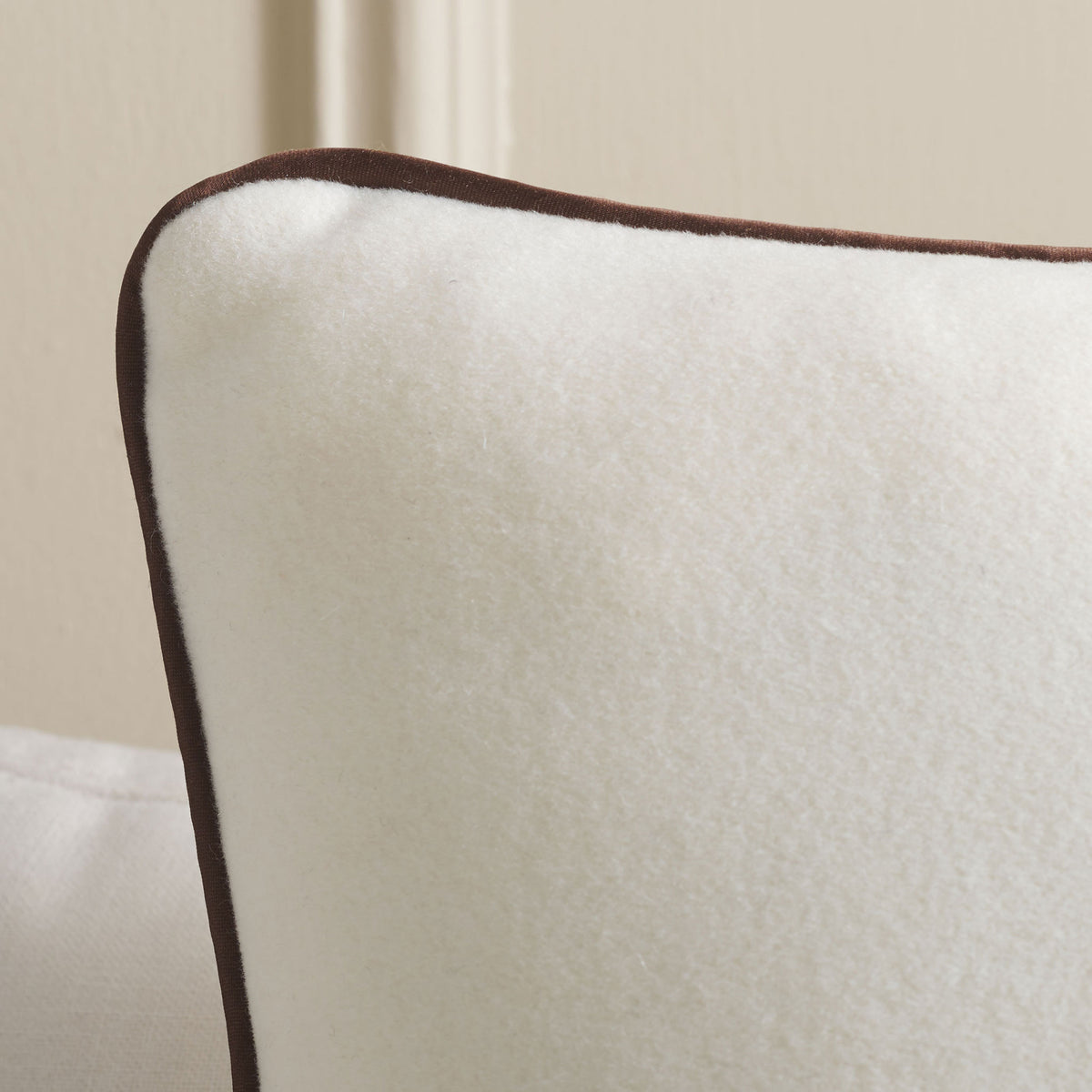 Soft ivory wool meets rich brown piping along the pillow's curved edge.
