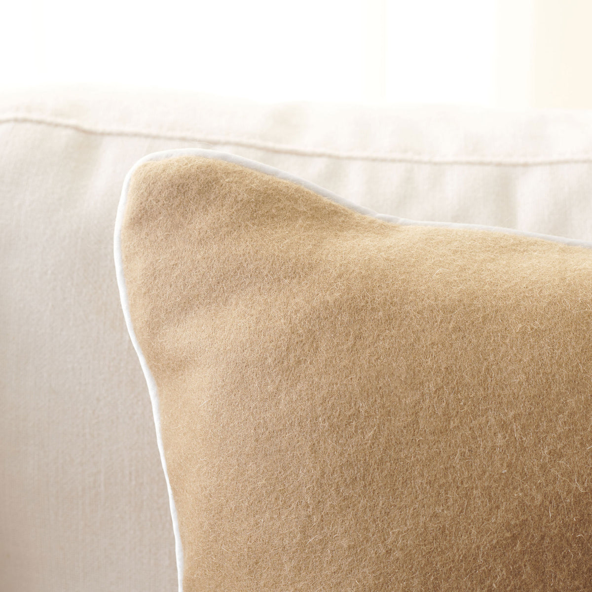 Soft camel wool meets delicate ivory piping along the pillow's curved edge.