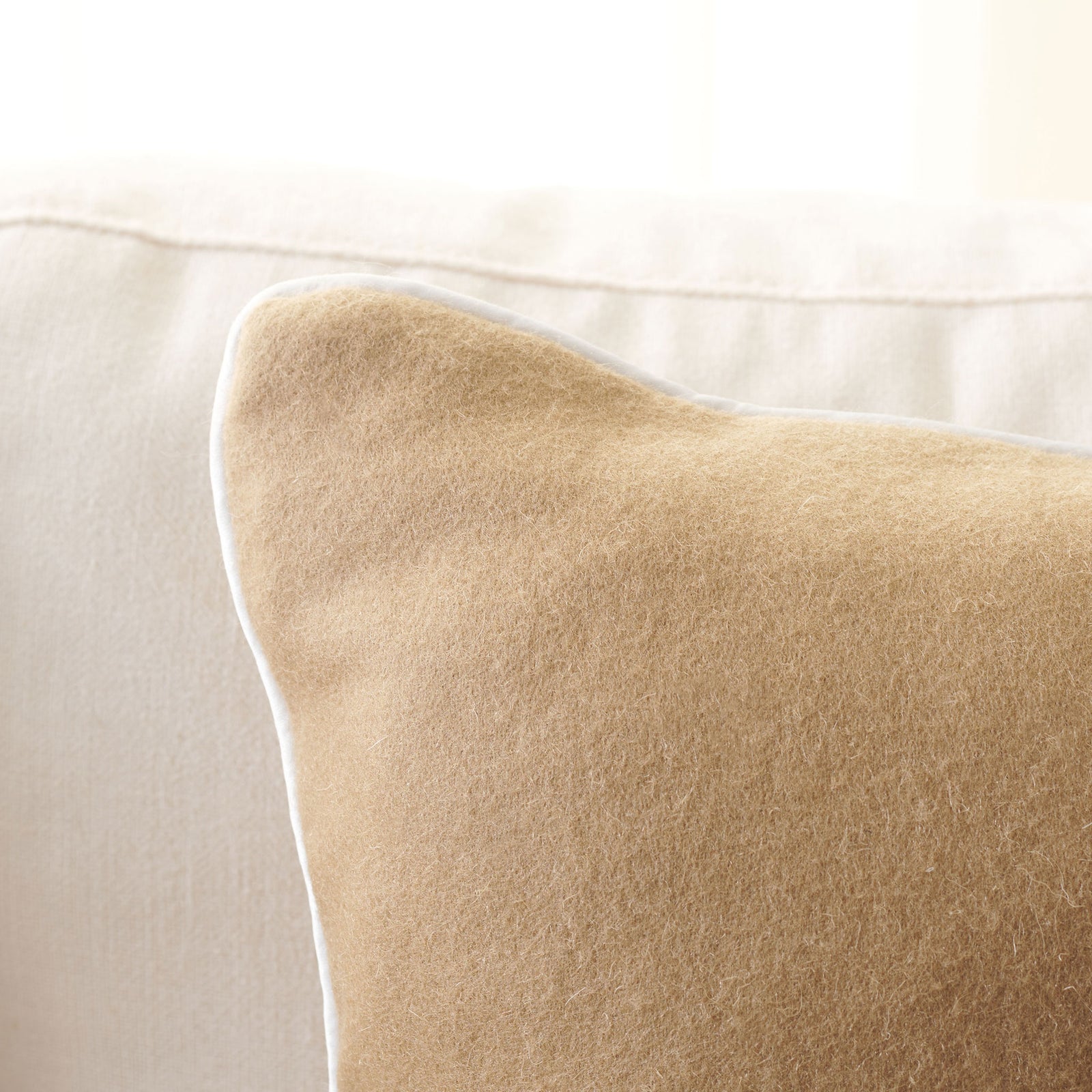 Soft camel wool meets delicate ivory piping along the pillow's curved edge. || PLS7223B-1818 || detail_room