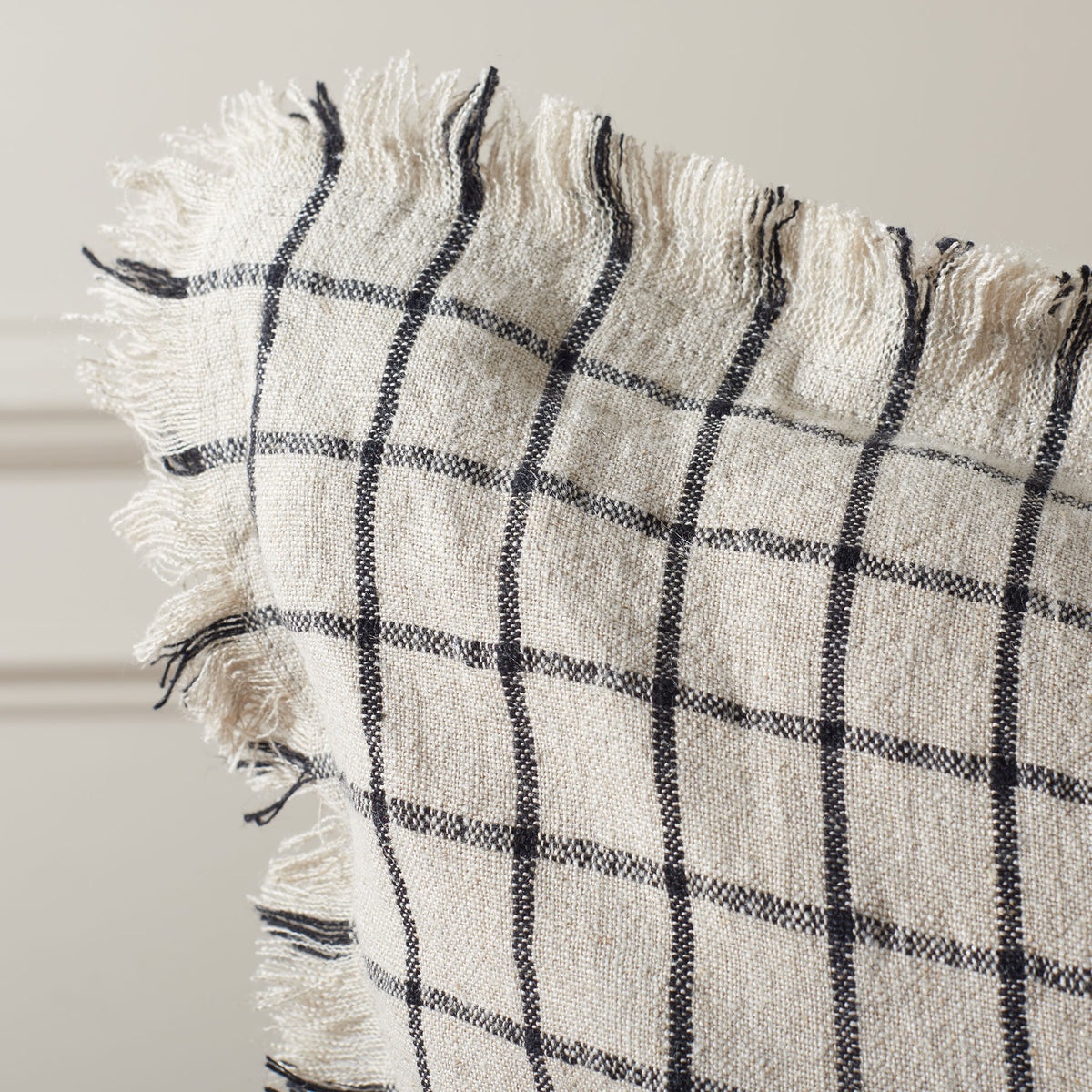 Wispy fringe and a textured weave soften the natural linen pillow's black grid || PLS8004A-2020 || detail_room